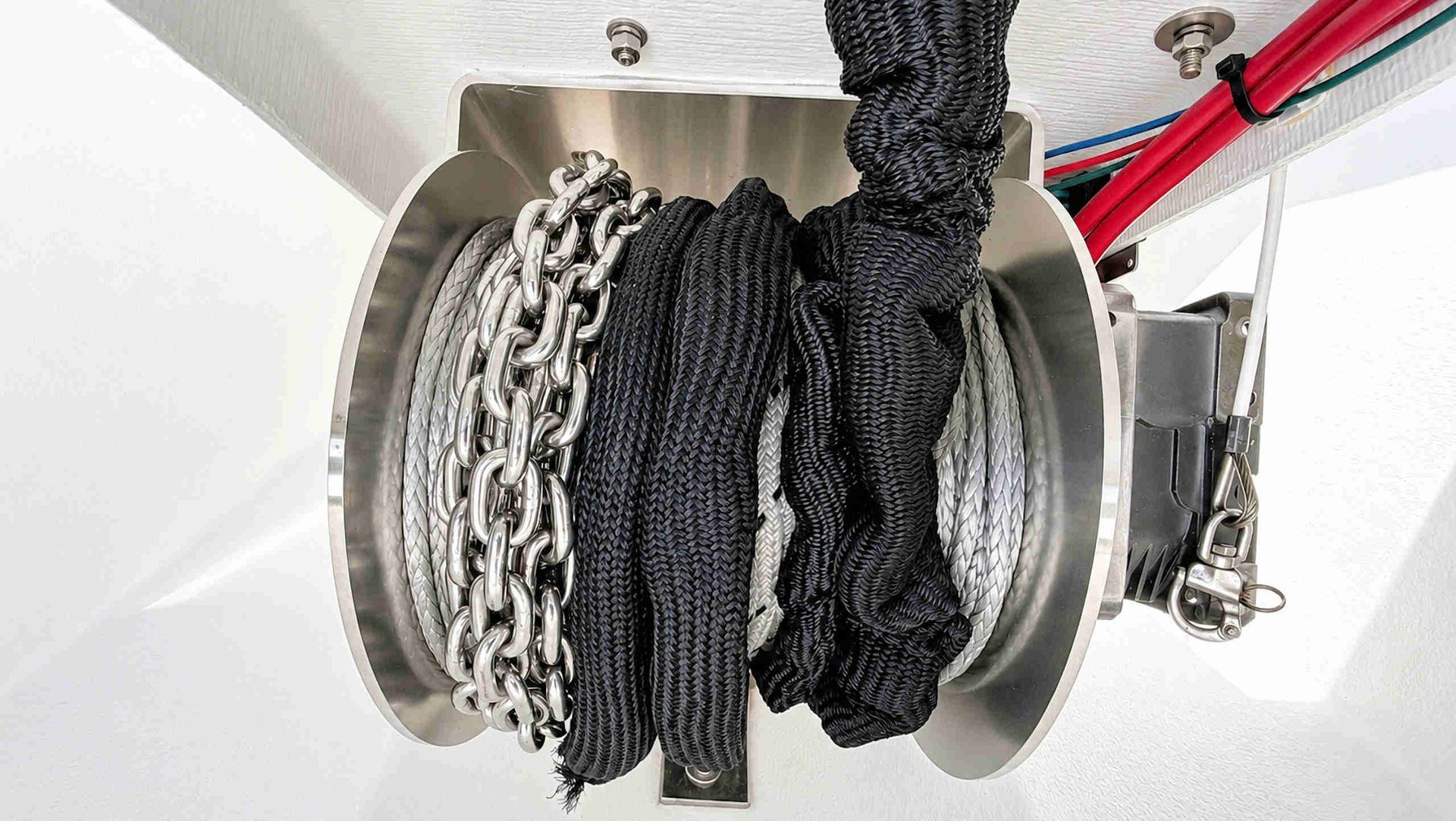 Coiled ropes and chains wound on a metal winch drum inside a white compartment