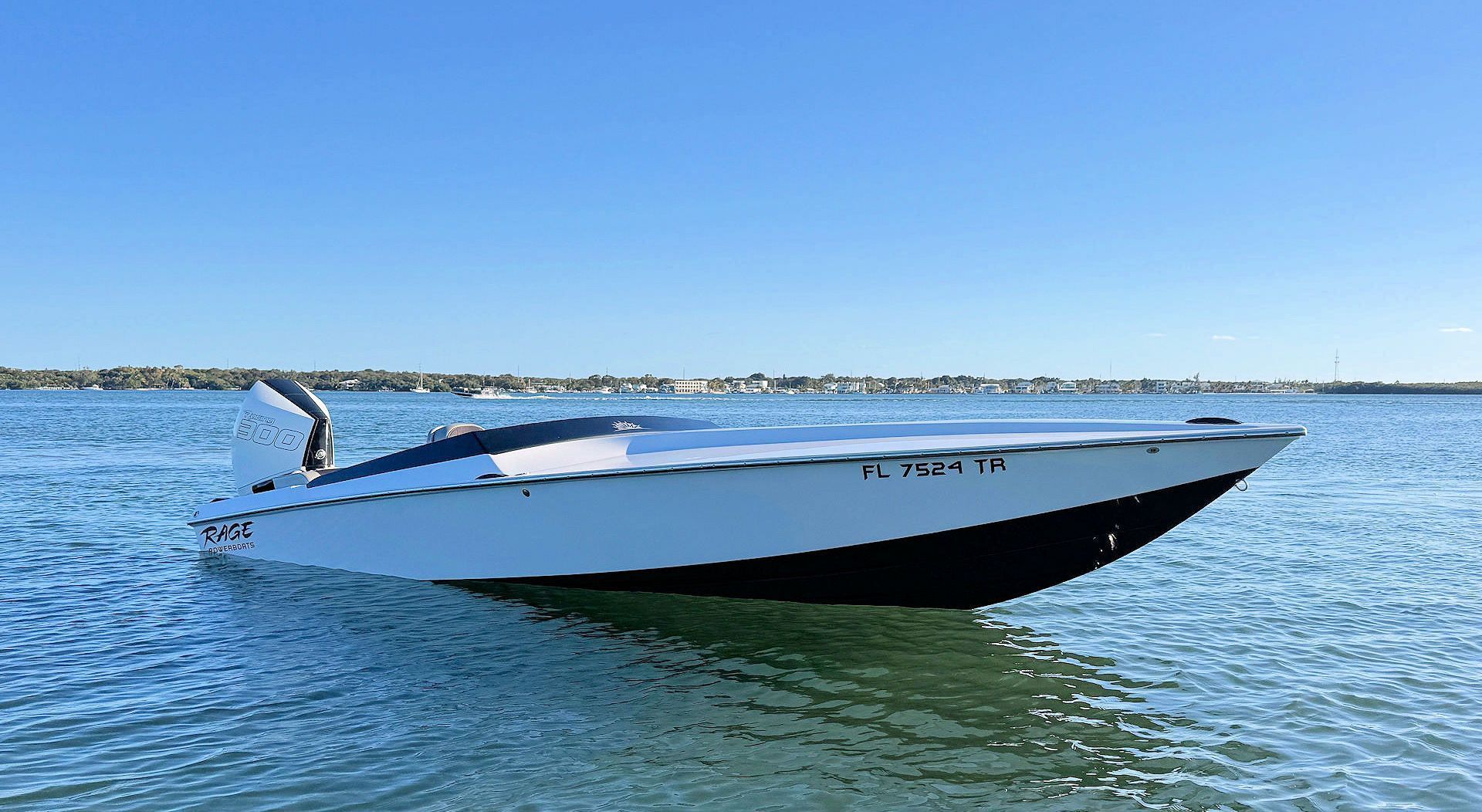 A sleek, white and dark-bottomed speedboat floating on calm, blue water under a clear sky.