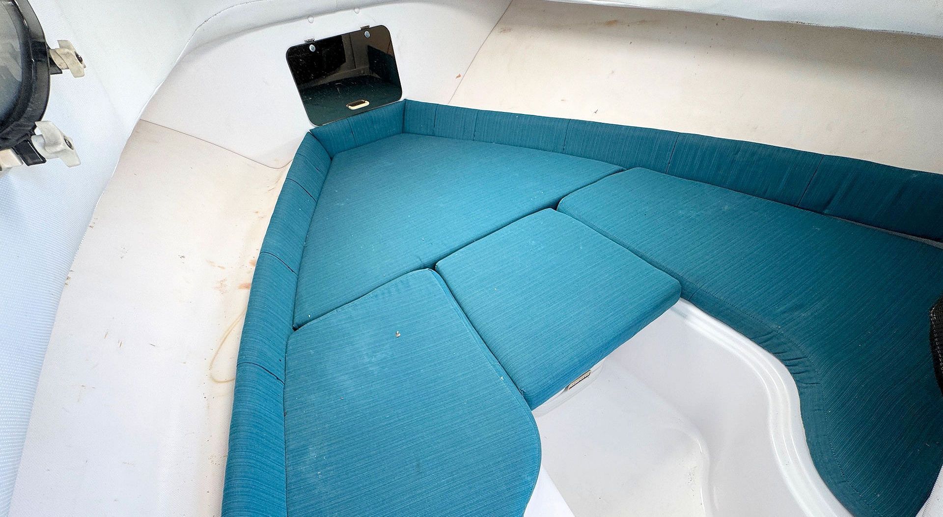A high-angle view of a boat's V-berth cabin, featuring teal cushioned seating arranged in a V-shape.