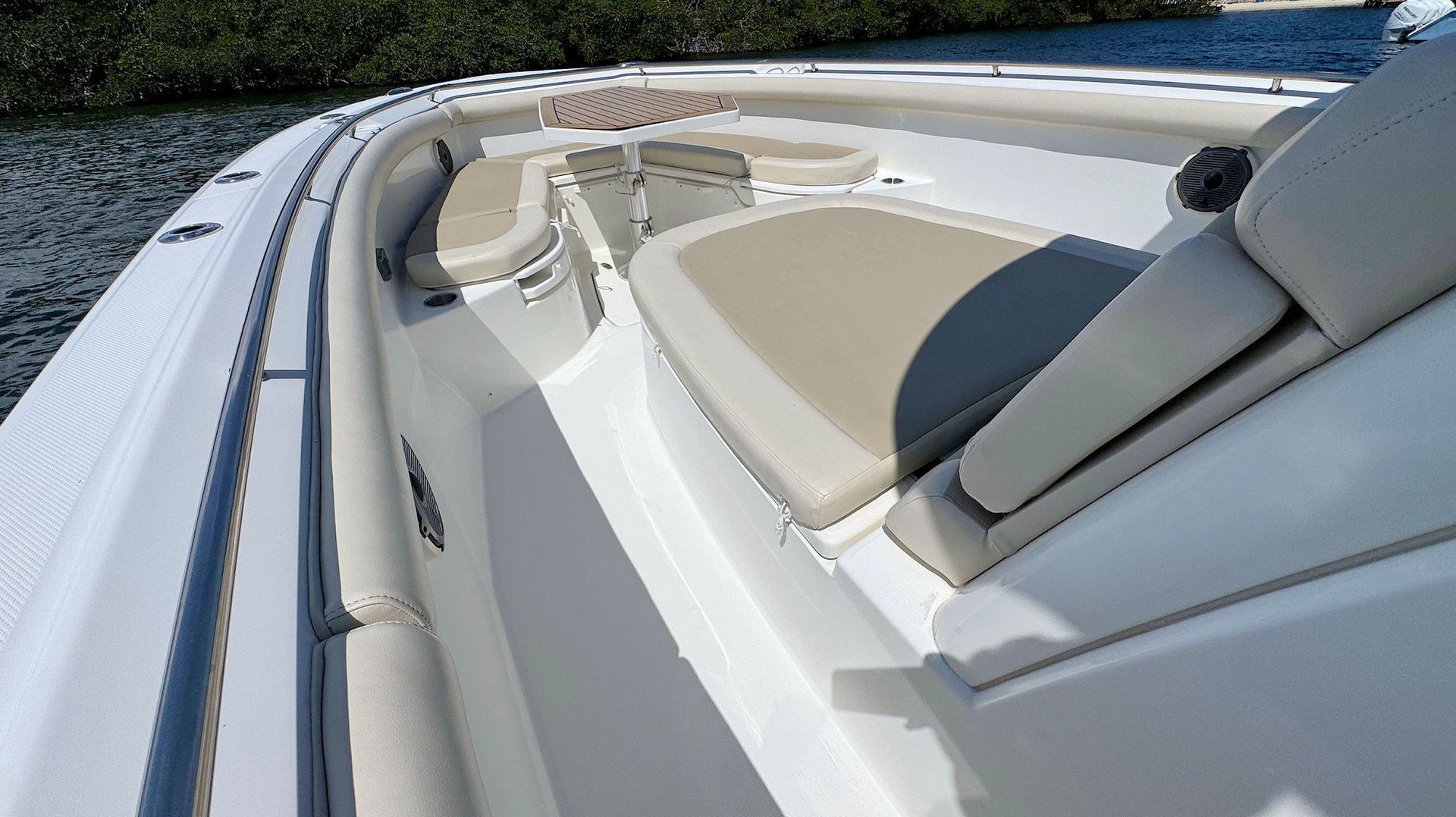 Close-up of a white boat deck with beige seating and stainless railing on the water.