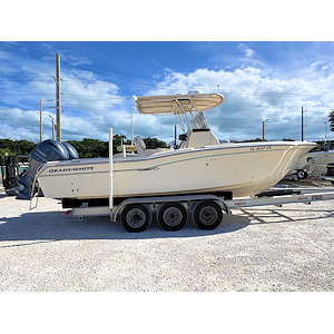 White speedboat on calm water with blue sky and light foliage in the background.