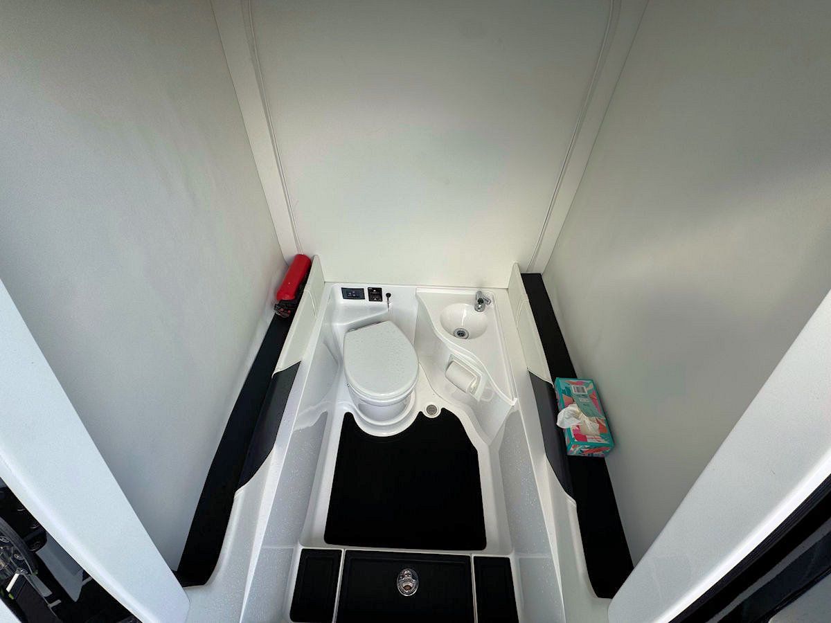 Boat's compact bathroom interior: white walls, toilet, sink, black flooring, and storage.
