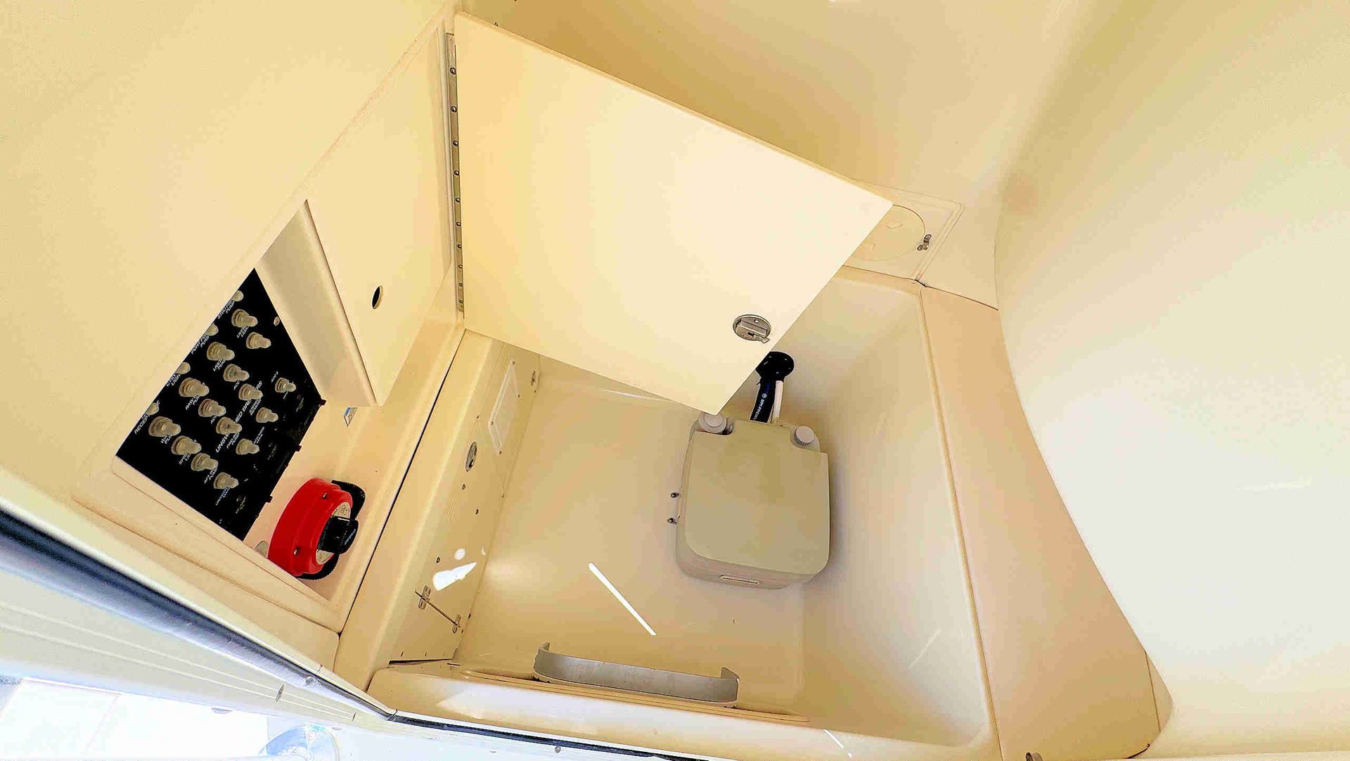 Small beige utility sink with faucet and drain, viewed from above inside a narrow cabinet.