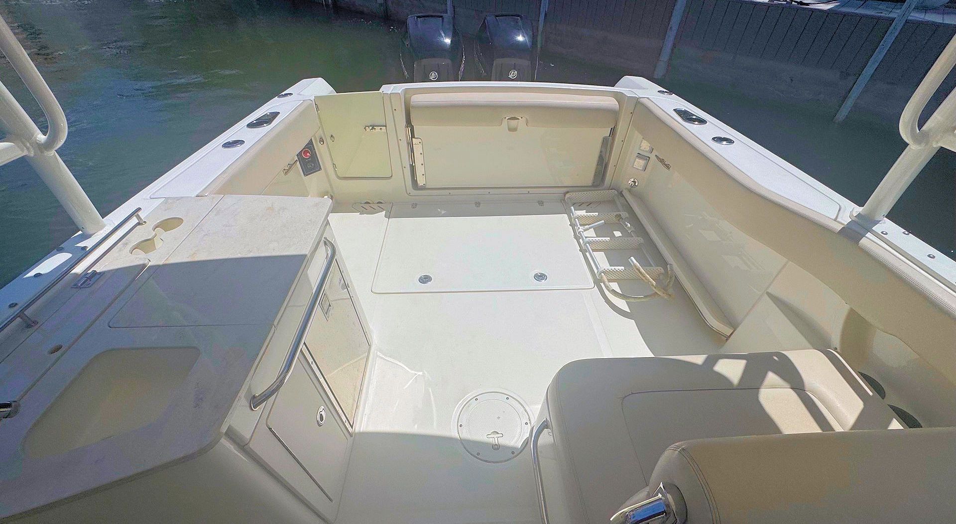 Rear view of an empty beige boat deck with seating, storage cabinets, and an open transom door overlooking the water.