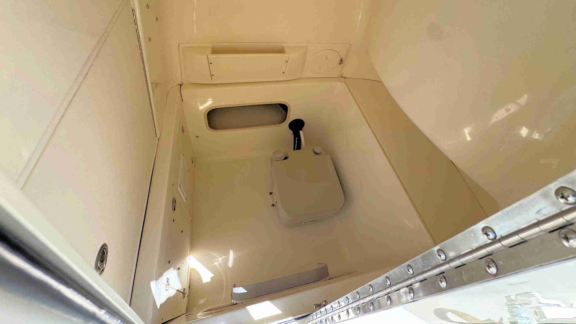 Interior of a small beige boat cabin with a hatch, window, and storage compartment.