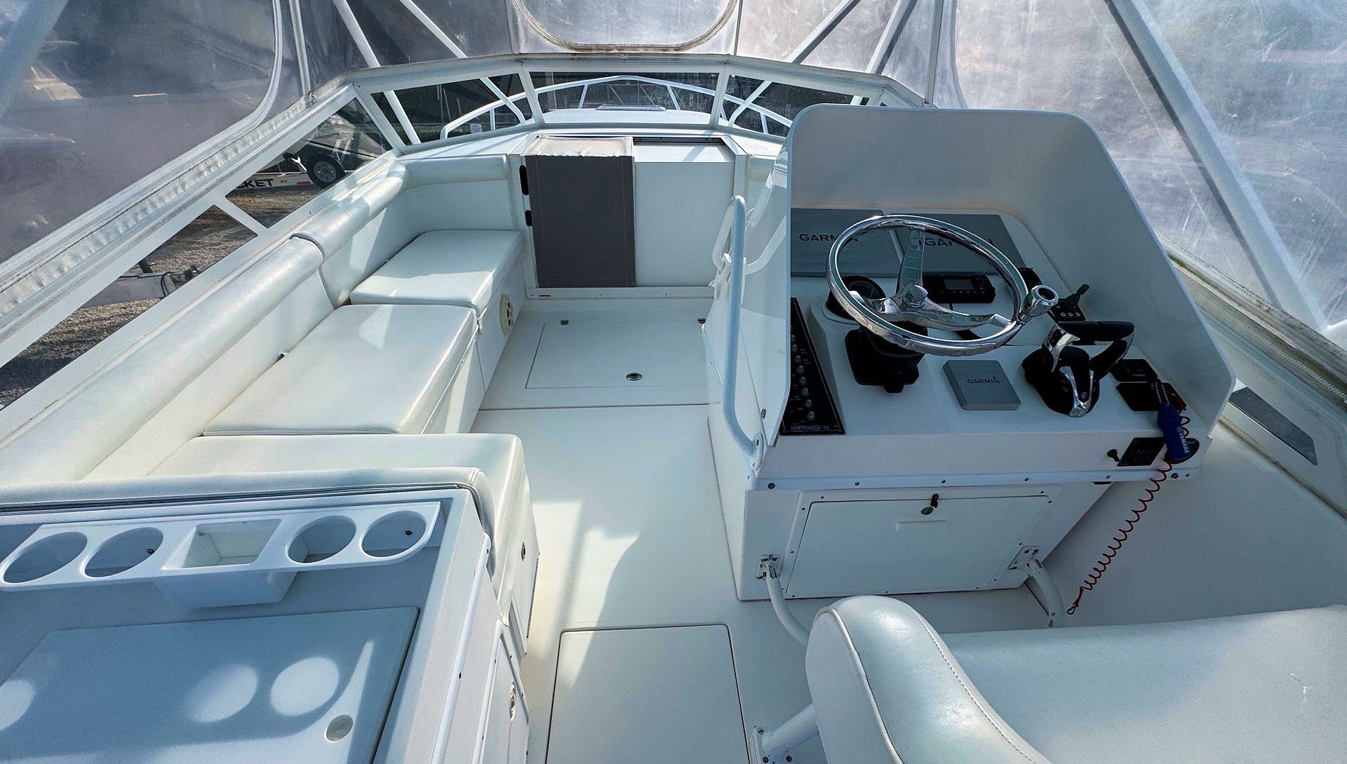 Empty boat cockpit with white seating, steering console, and cup holders under a clear canopy