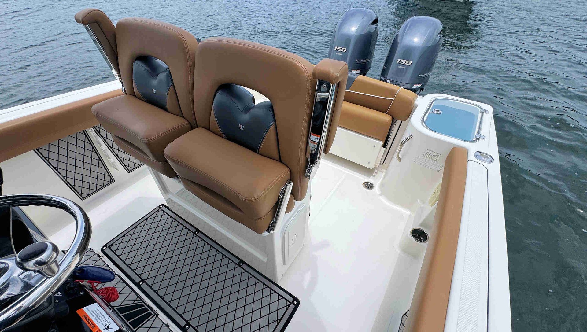 Boat cockpit with tan bench seats, helm wheel, and twin outboard motors on the water.