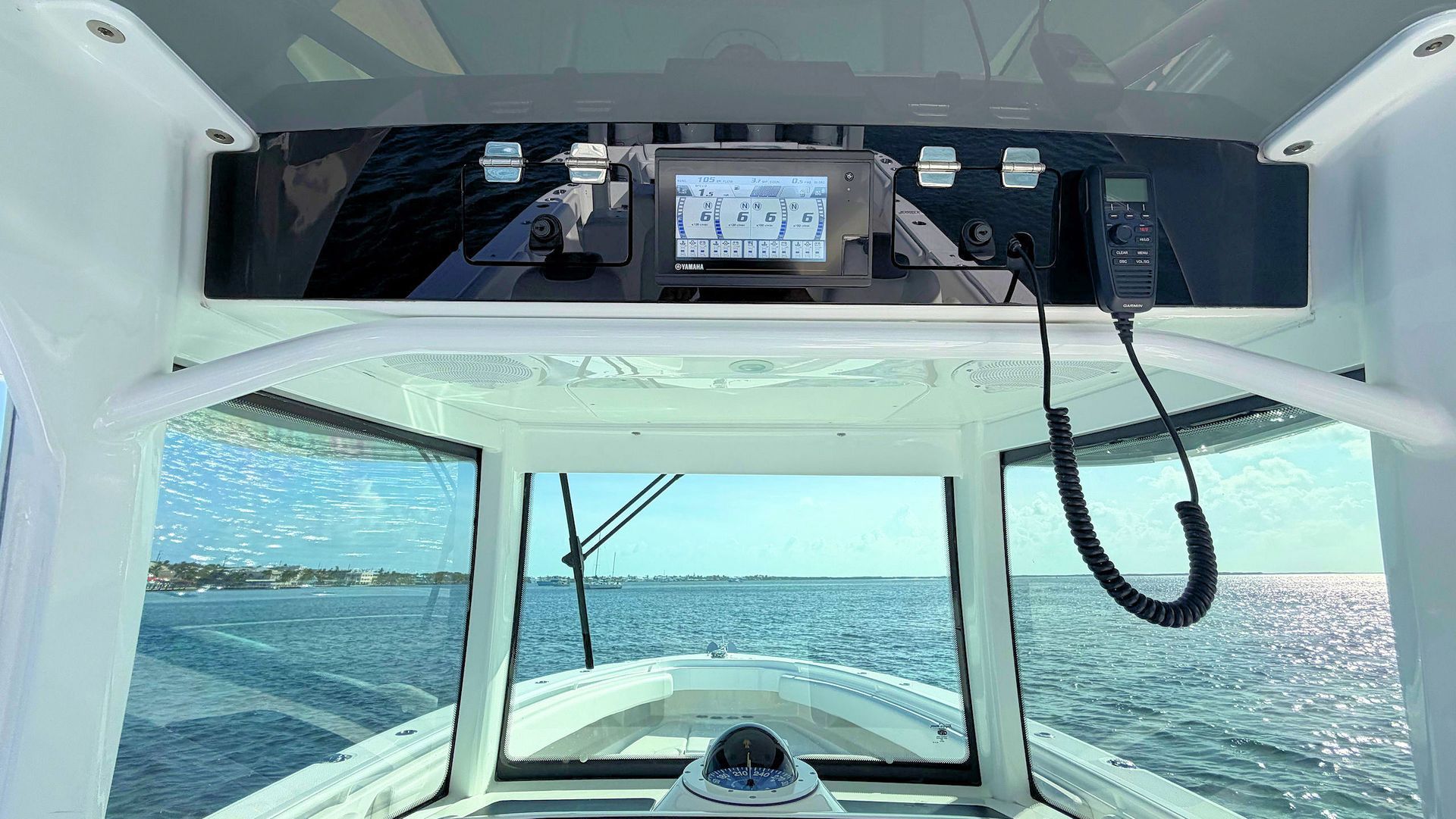 Overhead electronics viewed from boat cockpit, looking out over blue water through large windows and a white canopy.