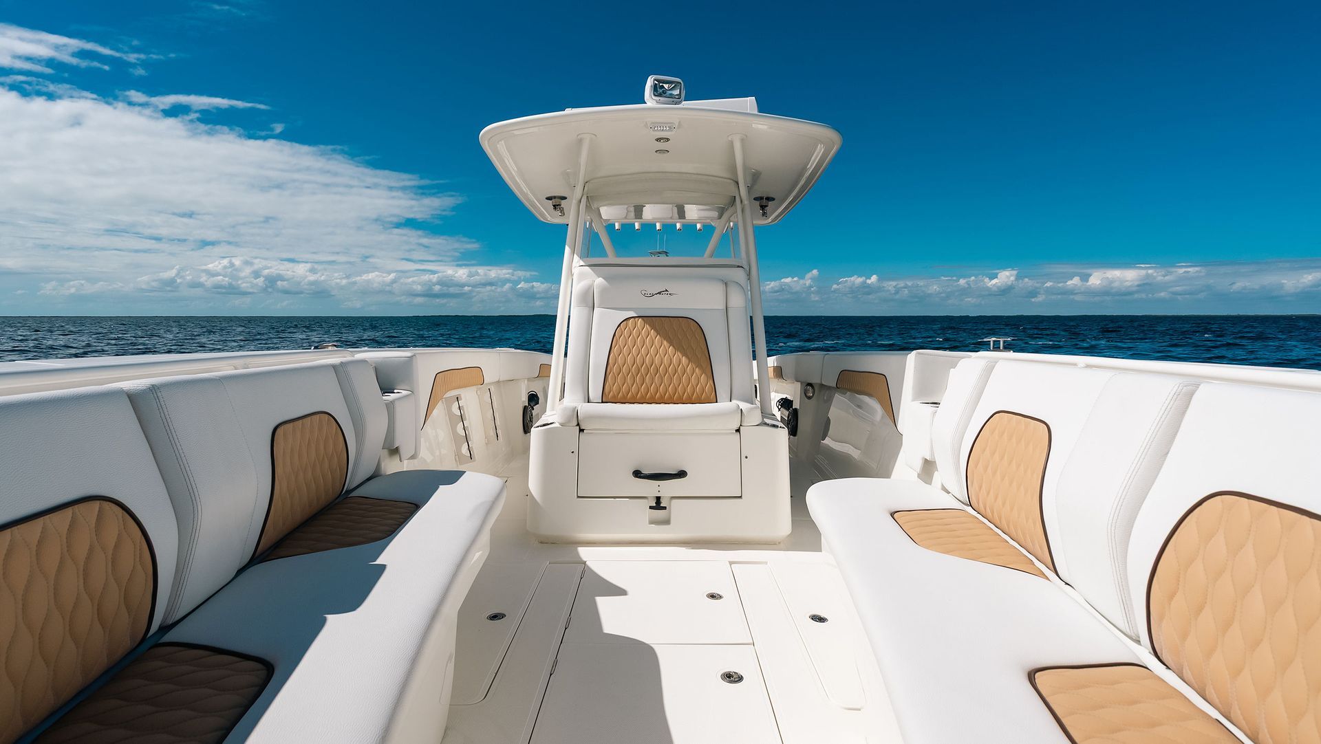 Luxury boat deck with white seating and tan cushions, facing open ocean under a blue sky