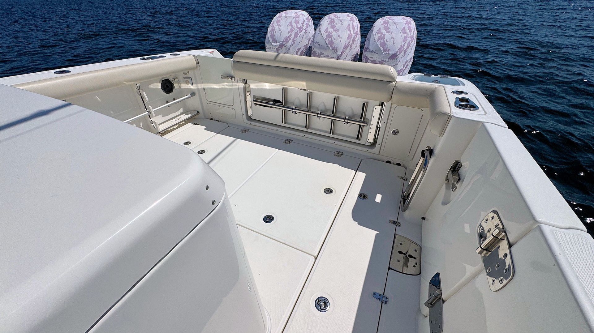 Boat cockpit with white seating, deck hatches, and ocean view behind three engine covers