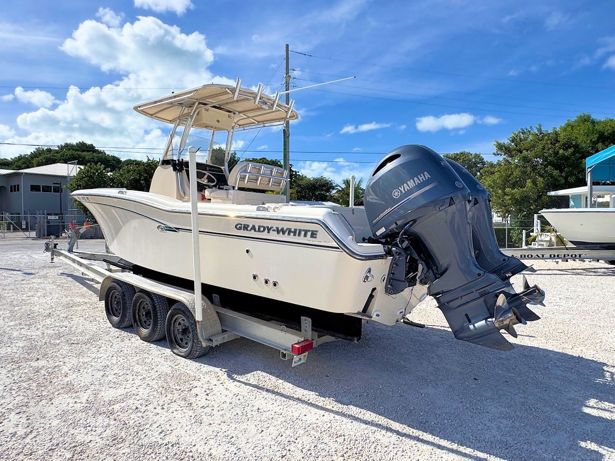 Cream-colored center console boat on a trailer, with two blue outboard motors, under a partly cloudy sky.