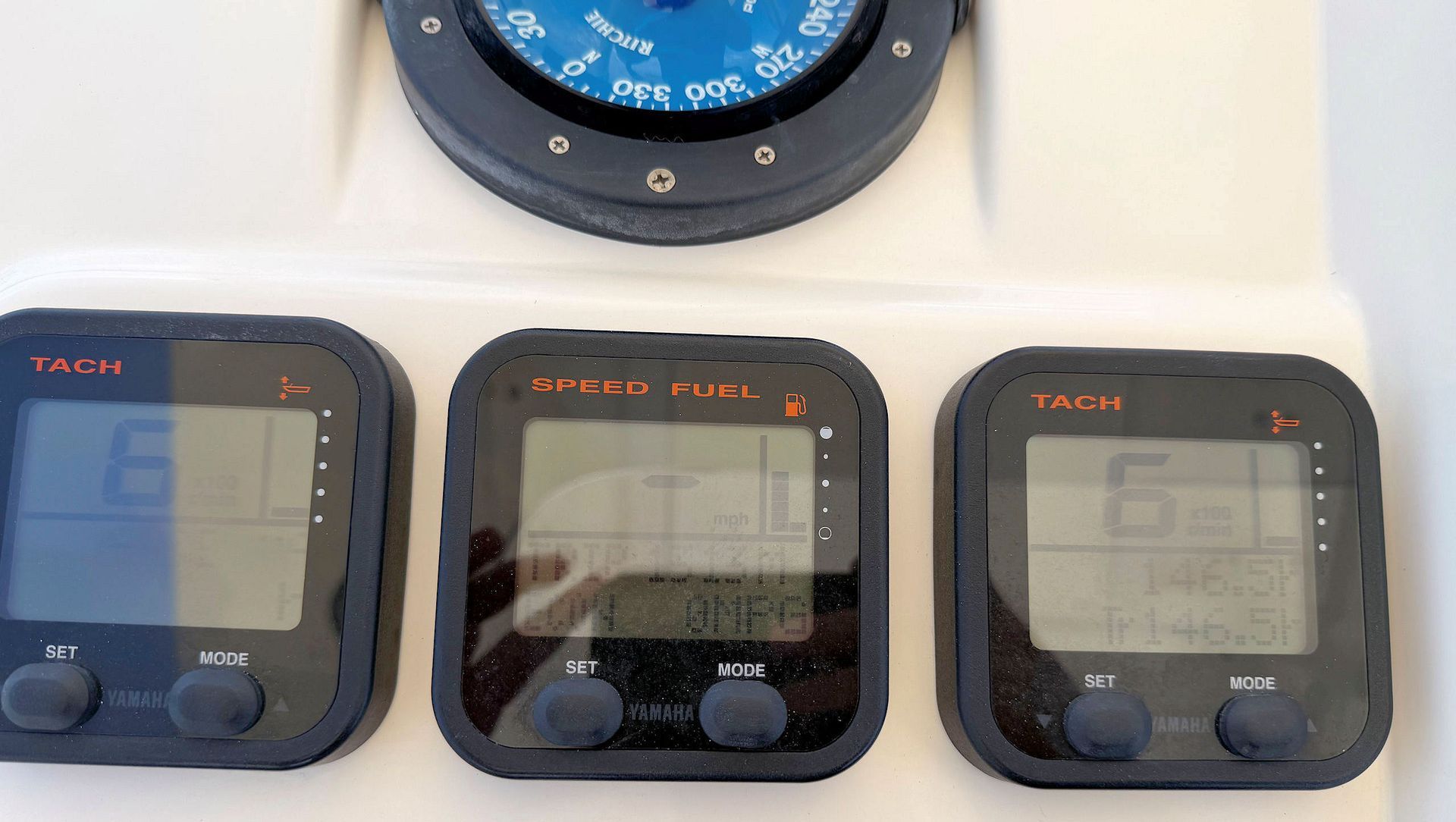 Three black marine instrument displays mounted on a beige panel, with a round blue gauge above them.
