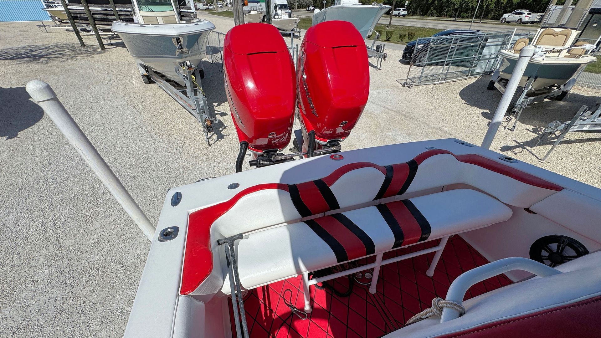 Red motorboat with twin outboard engines on a rocky shore, viewed from the deck with a white bench seat.