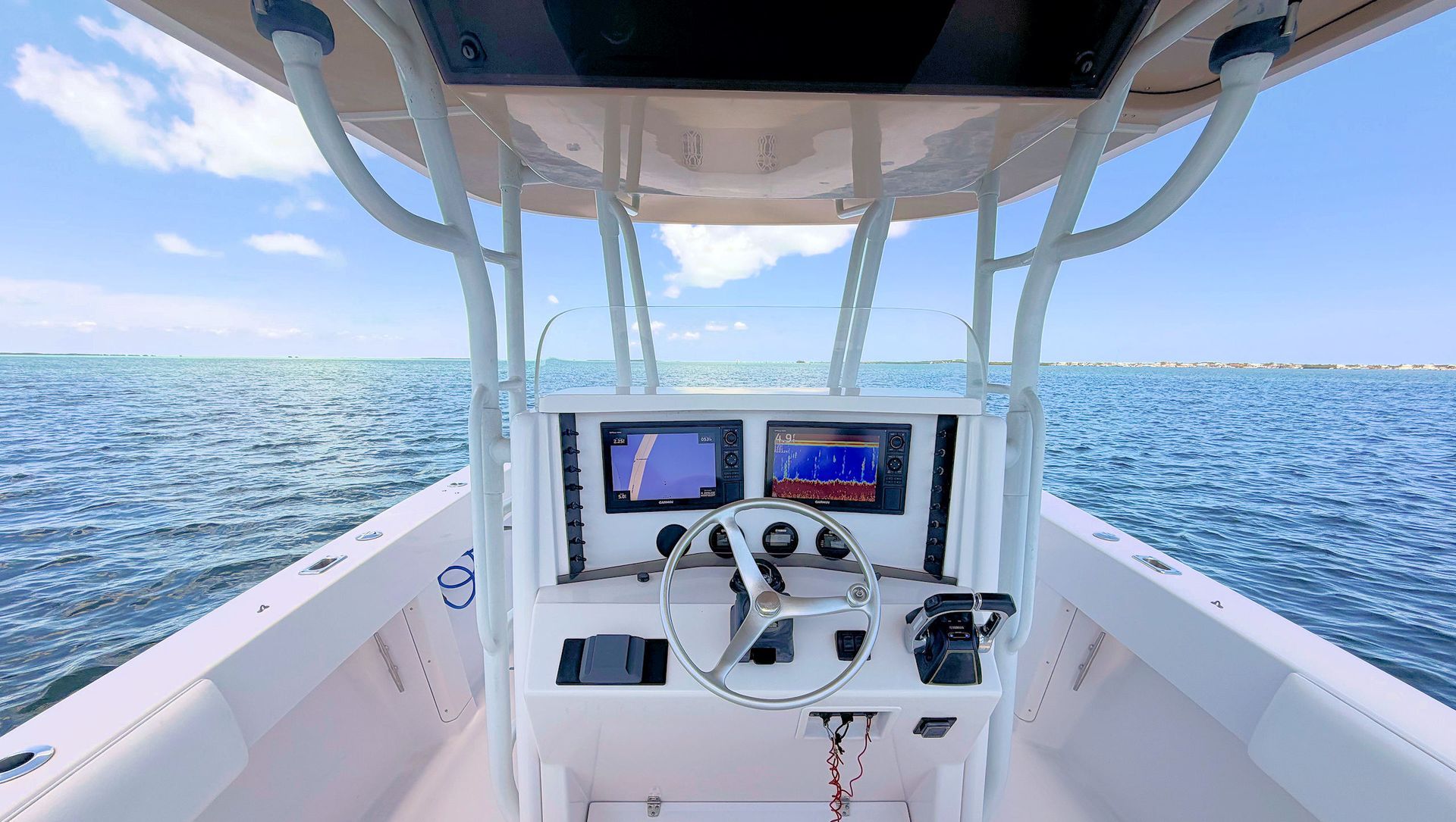Boat helm with two displays overlooking open blue ocean under a canopy