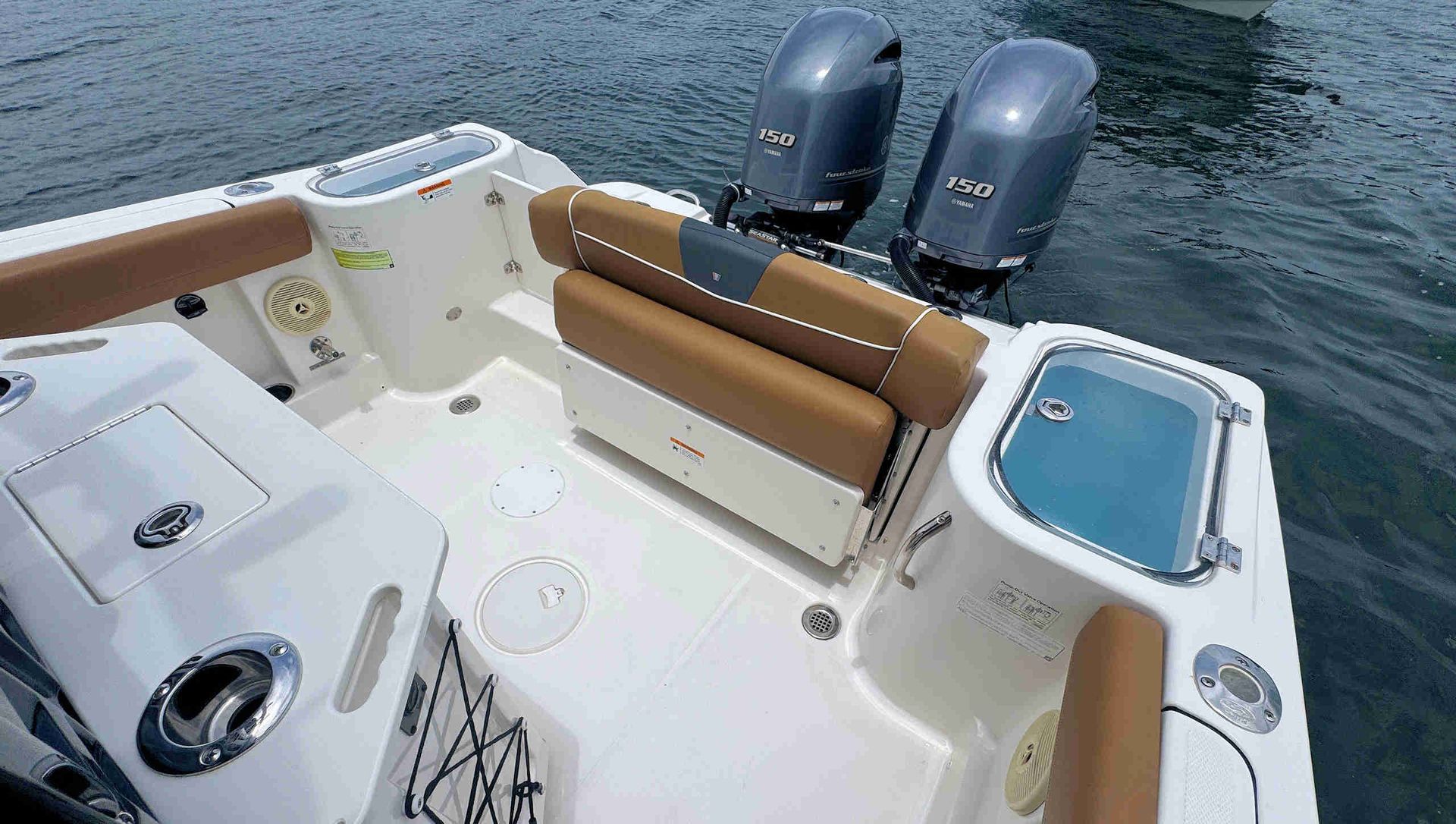 Boat stern with tan seating, white deck, and two gray outboard motors on the water