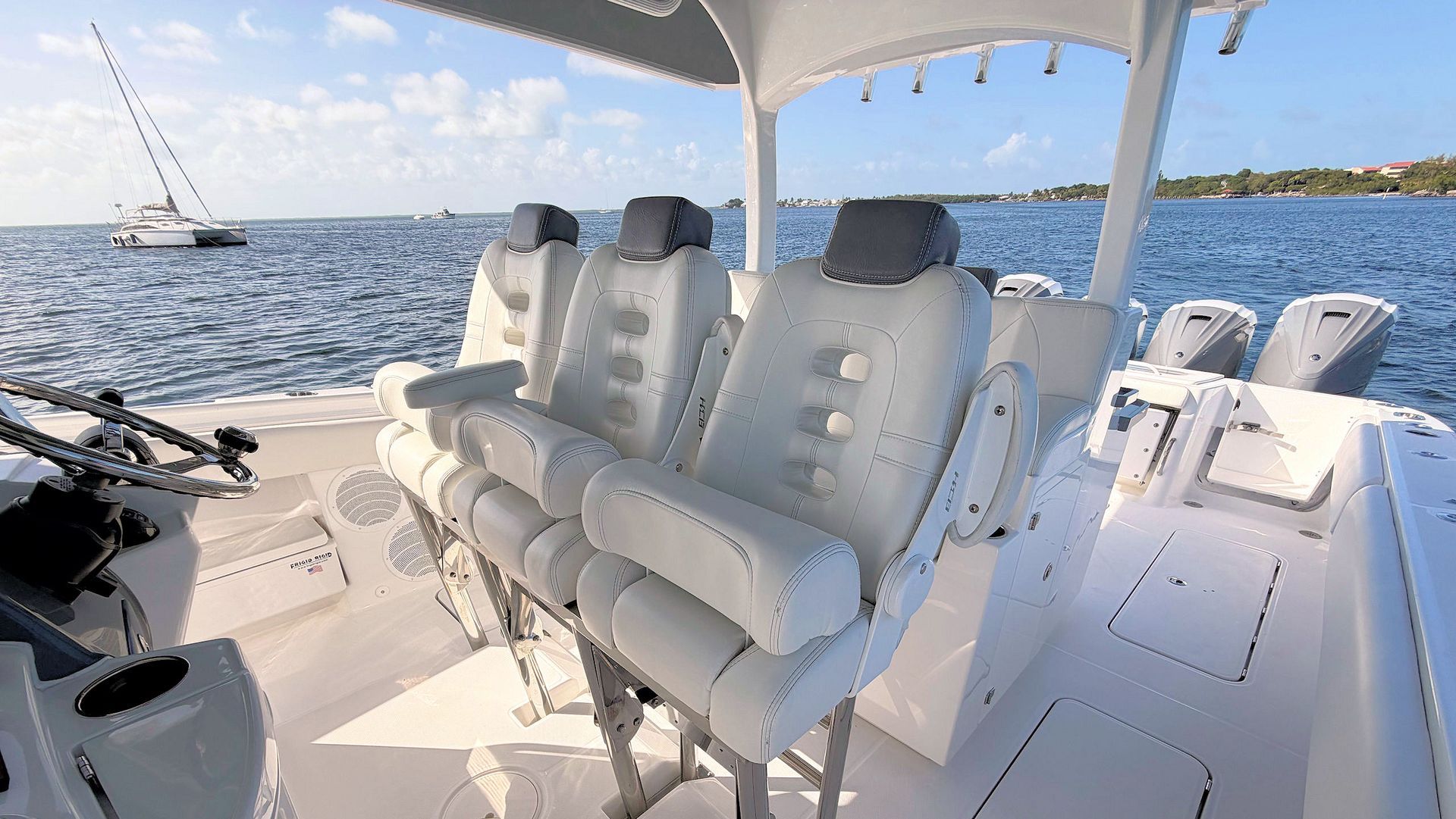 White captains chairs under a large t-top on a sunny yacht, with ocean and sailboats in the background