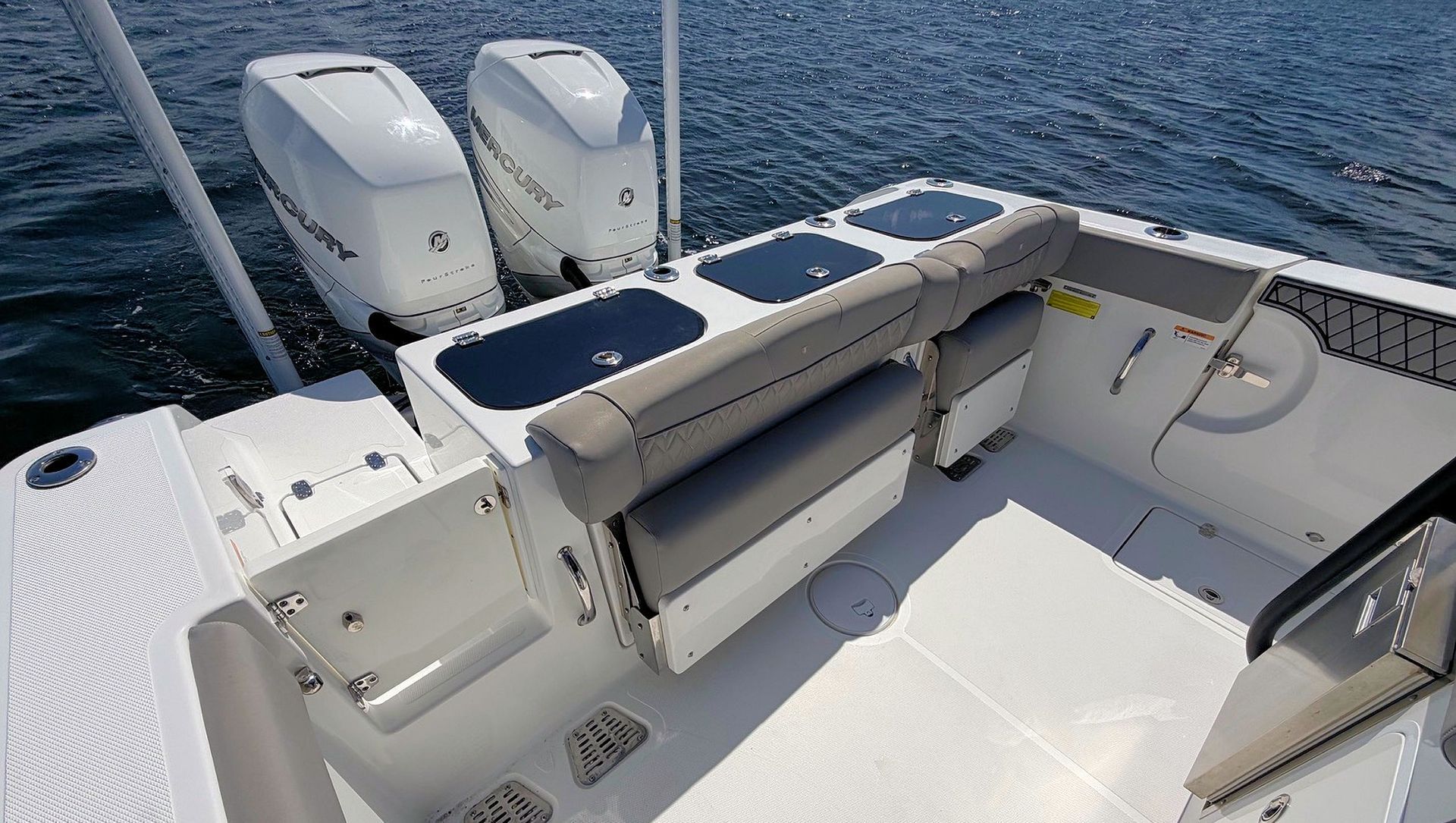 White boat deck with gray bench seating, twin outboard motors, and blue ocean in the background