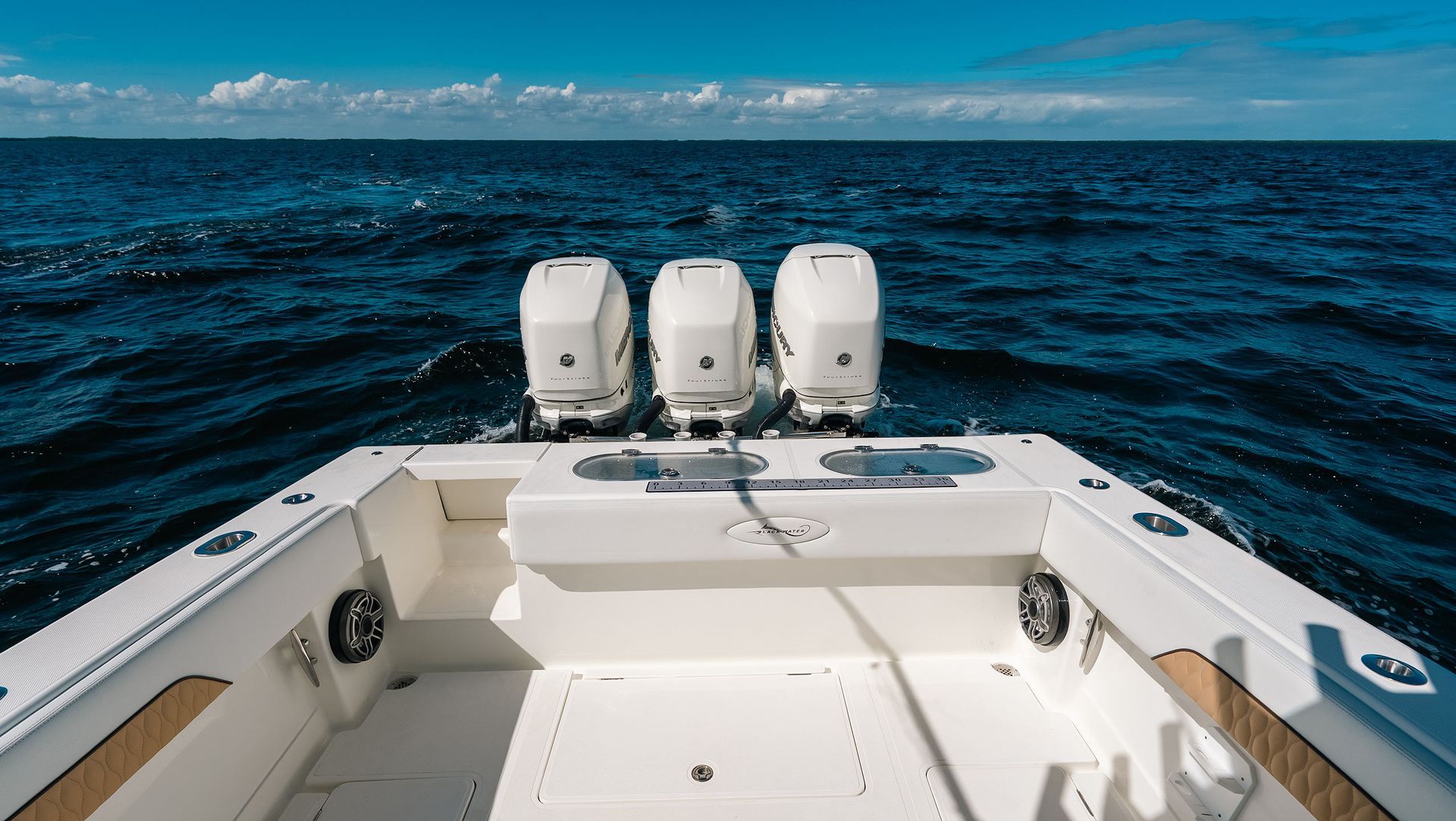 Boat stern with three outboard motors on open ocean under a blue sky
