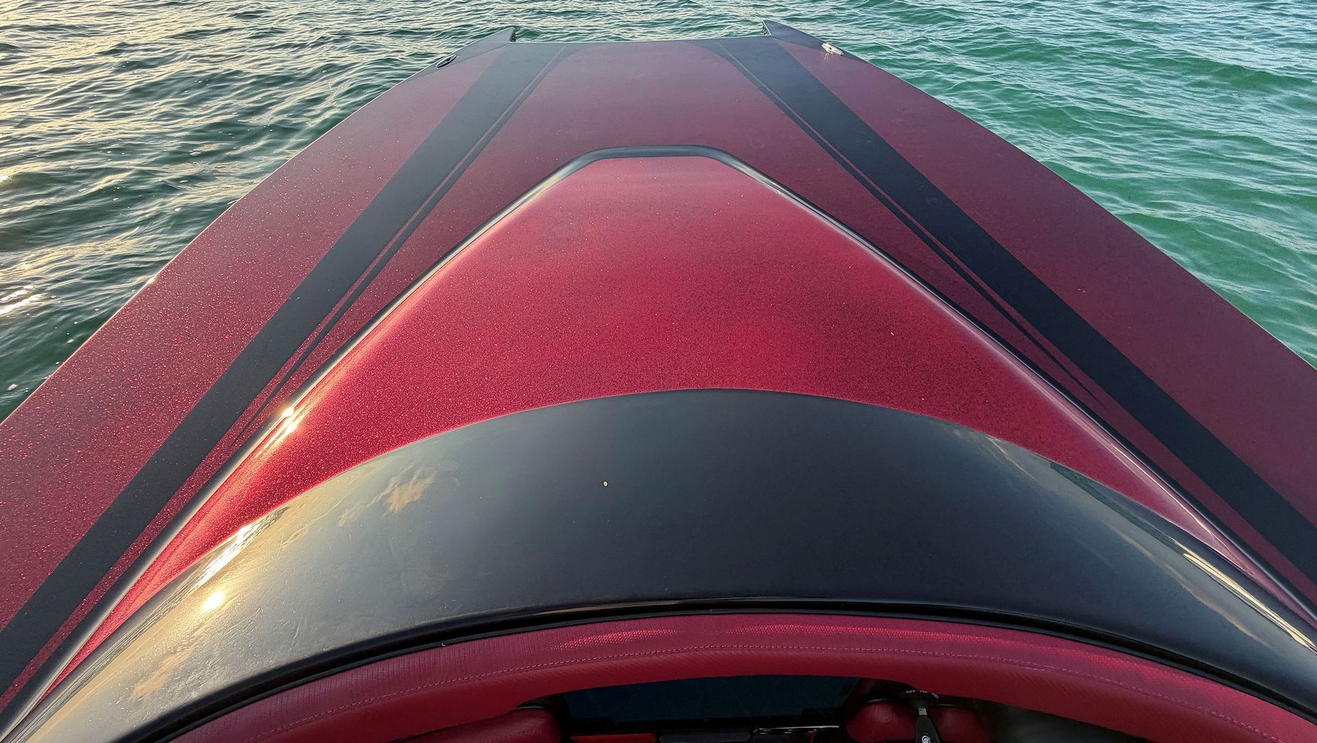 Red high-performance catamaran bow cutting through water, with a black center panel and red deck.
