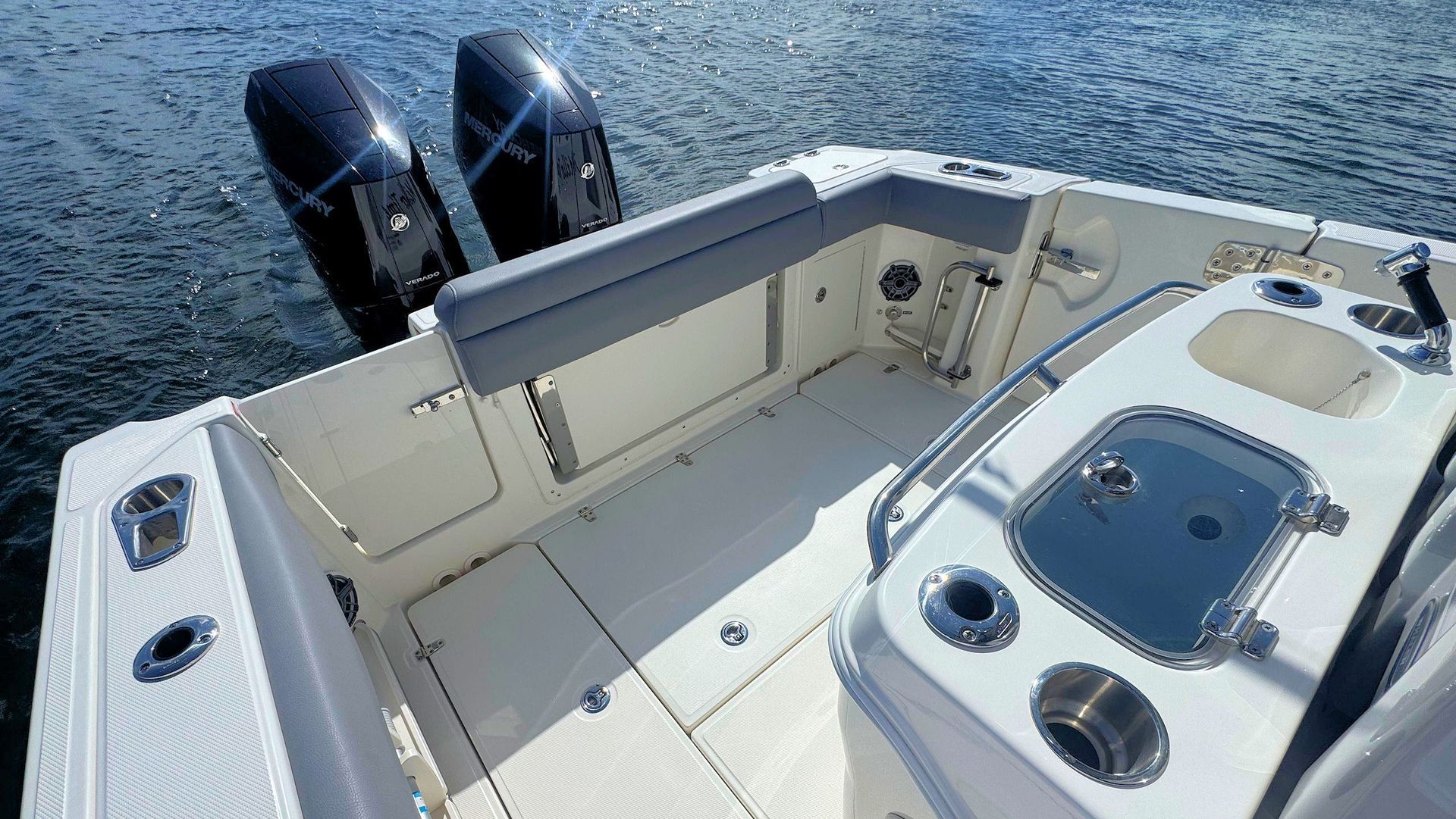 An overhead, rear view of the cockpit of a Boston Whaler boat, featuring beige flooring, gray bench seating, and dual outboard motors.