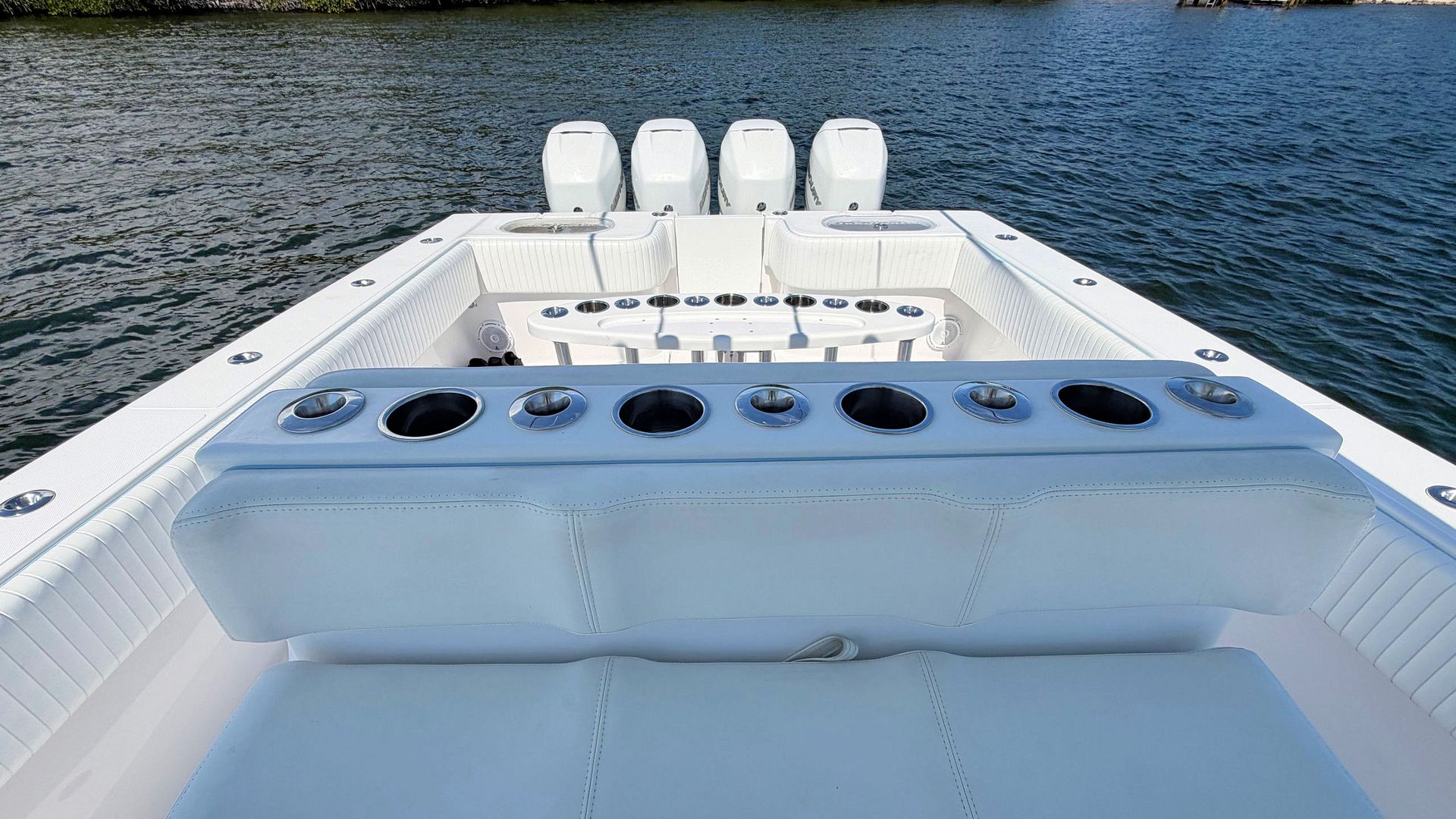 White fishing boat deck with rod holders and four outboard engines on calm water, viewed from the stern