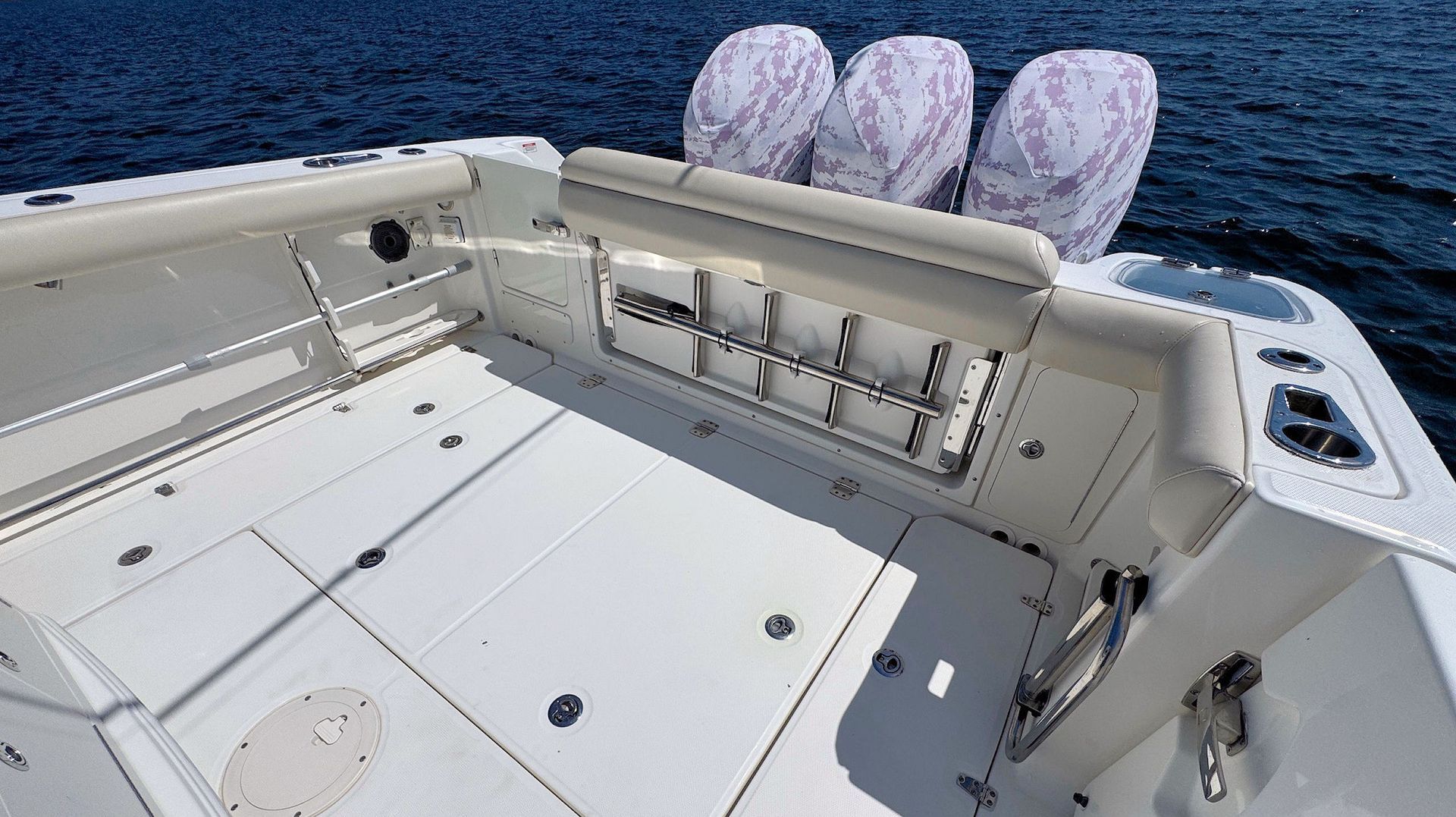 Boat deck with white seating and three cushioned chairs overlooking blue water