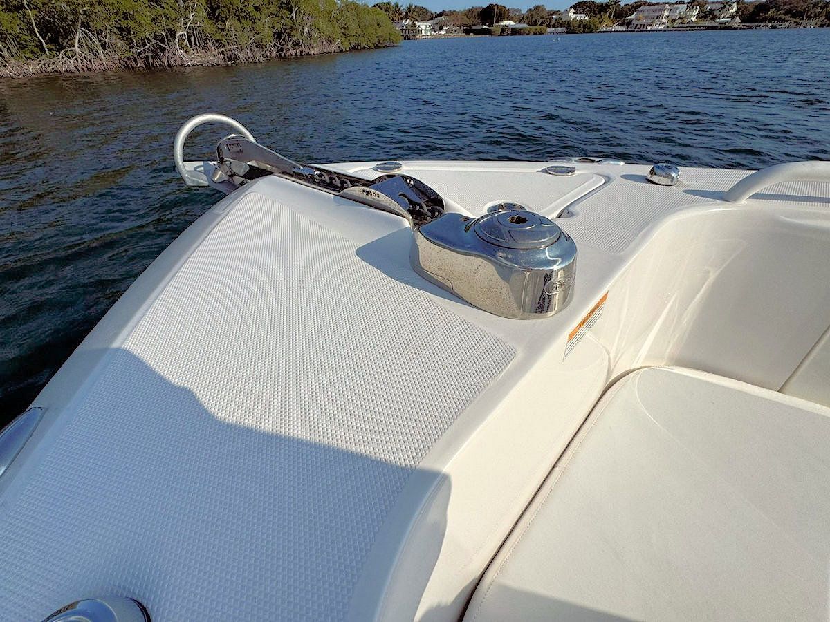 White boat bow with anchor, chrome windlass, and water in the background.
