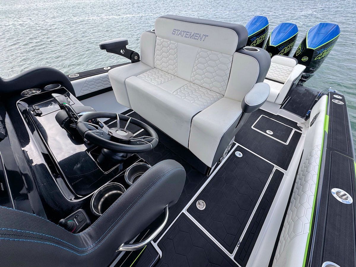 High-speed boat cockpit with black and white seating, steering wheel, and four blue outboard motors.