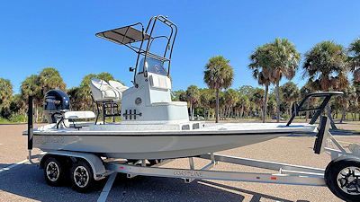 Gray fishing boat on a trailer, with a blue sky and palm trees in the background.