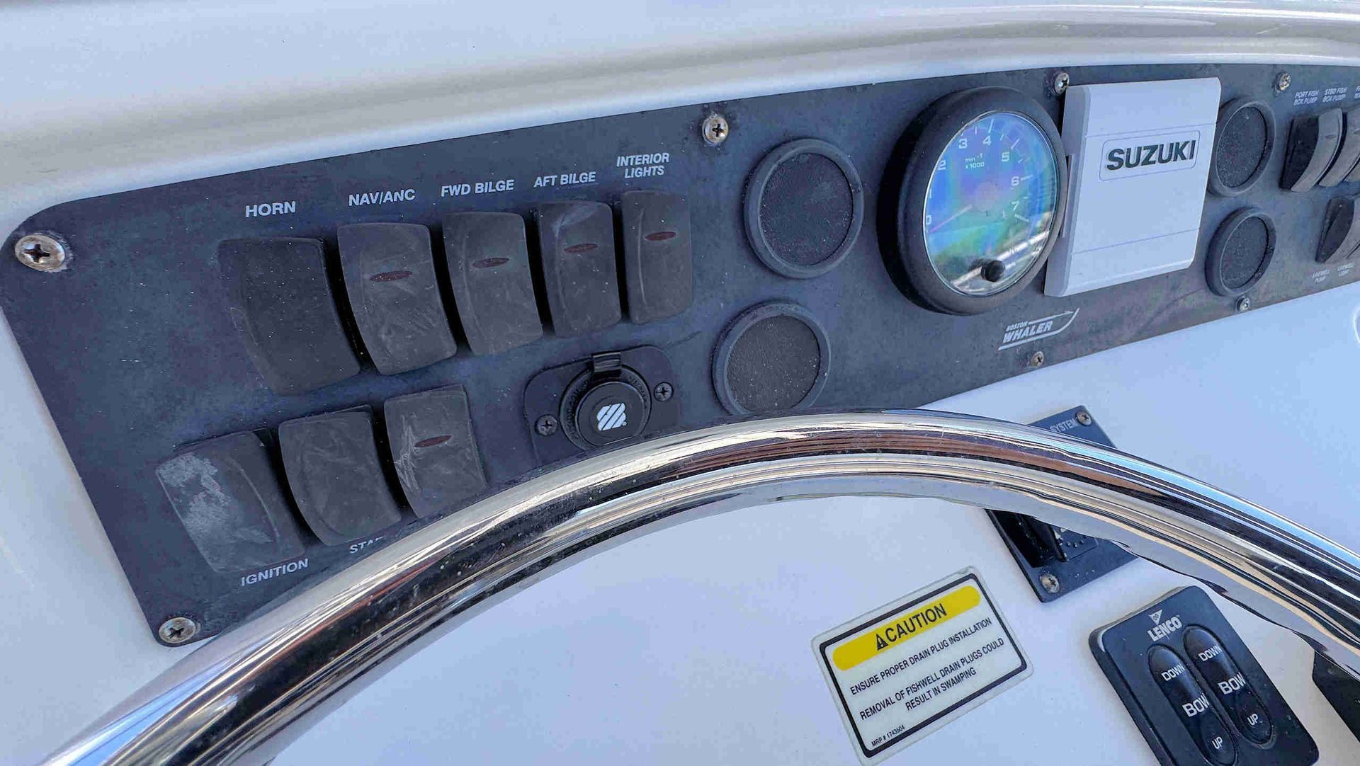 Close-up of a boat dashboard with switches, gauges, and a steering wheel in the foreground.