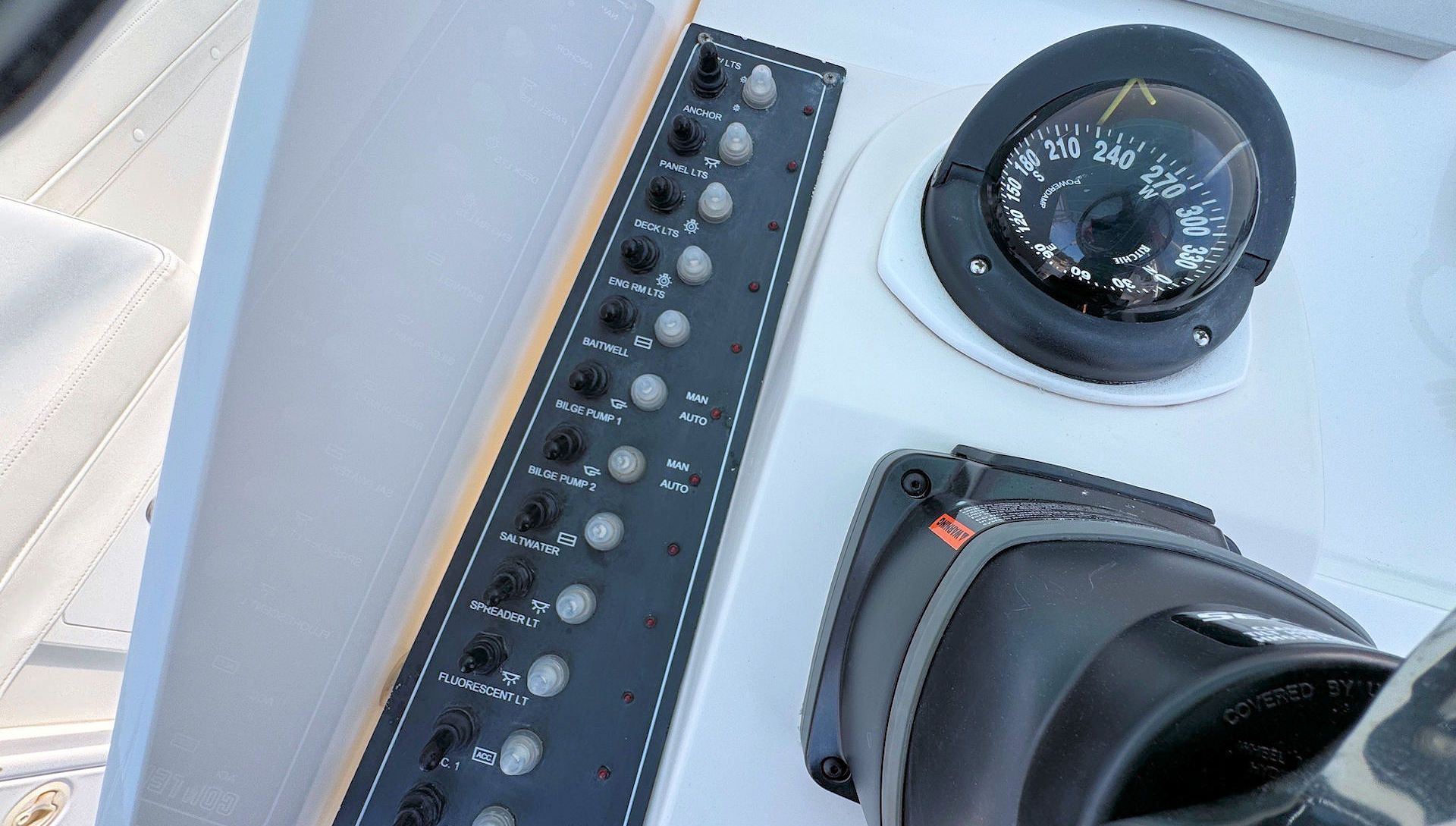Boat helm console with throttle switches and a compass next to a steering wheel