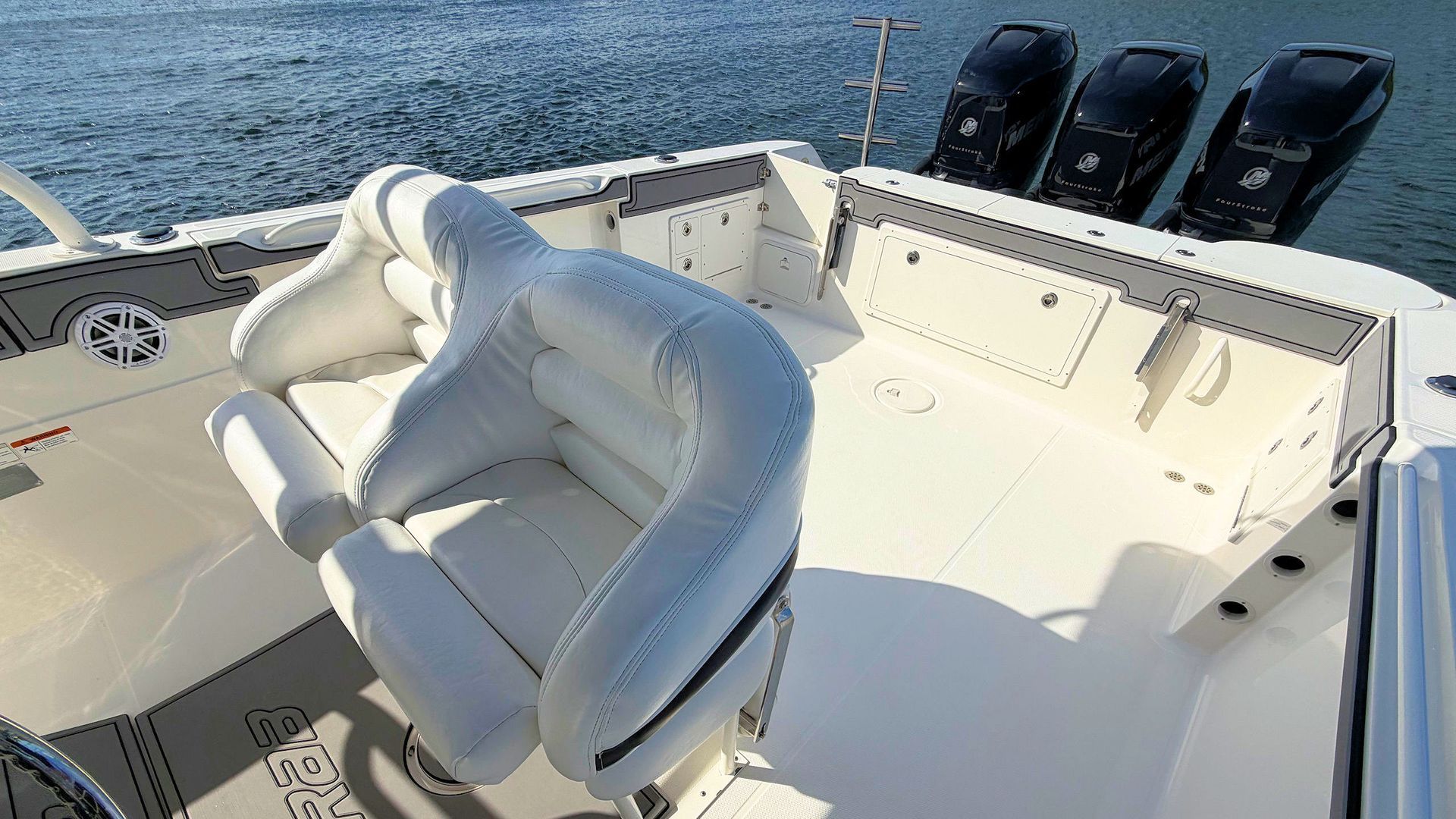 White captain’s chair on a boat deck with ocean water and three black seats in the background