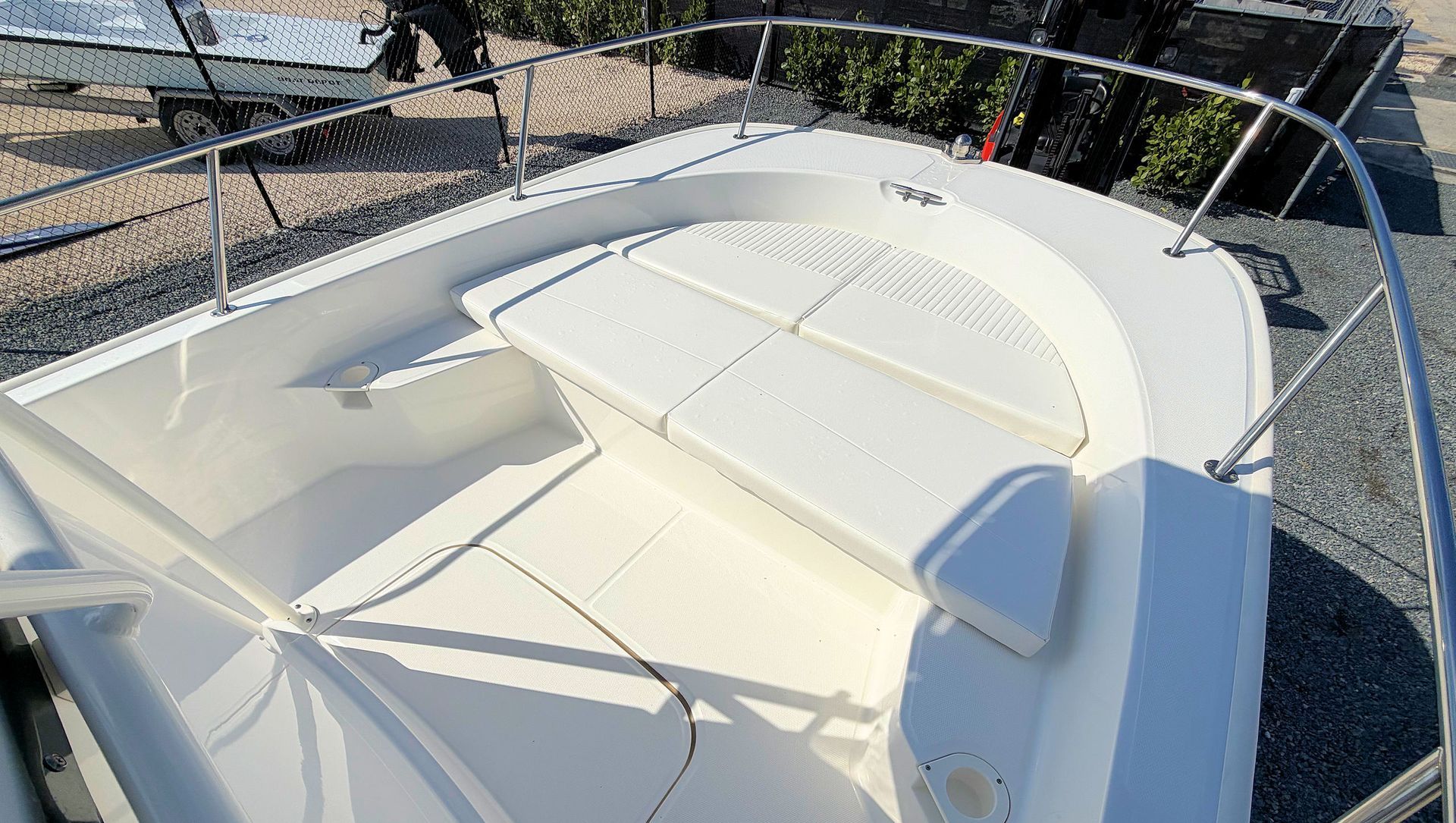 White cushioned boat seating on a deck, viewed through a metal railing in bright sunlight