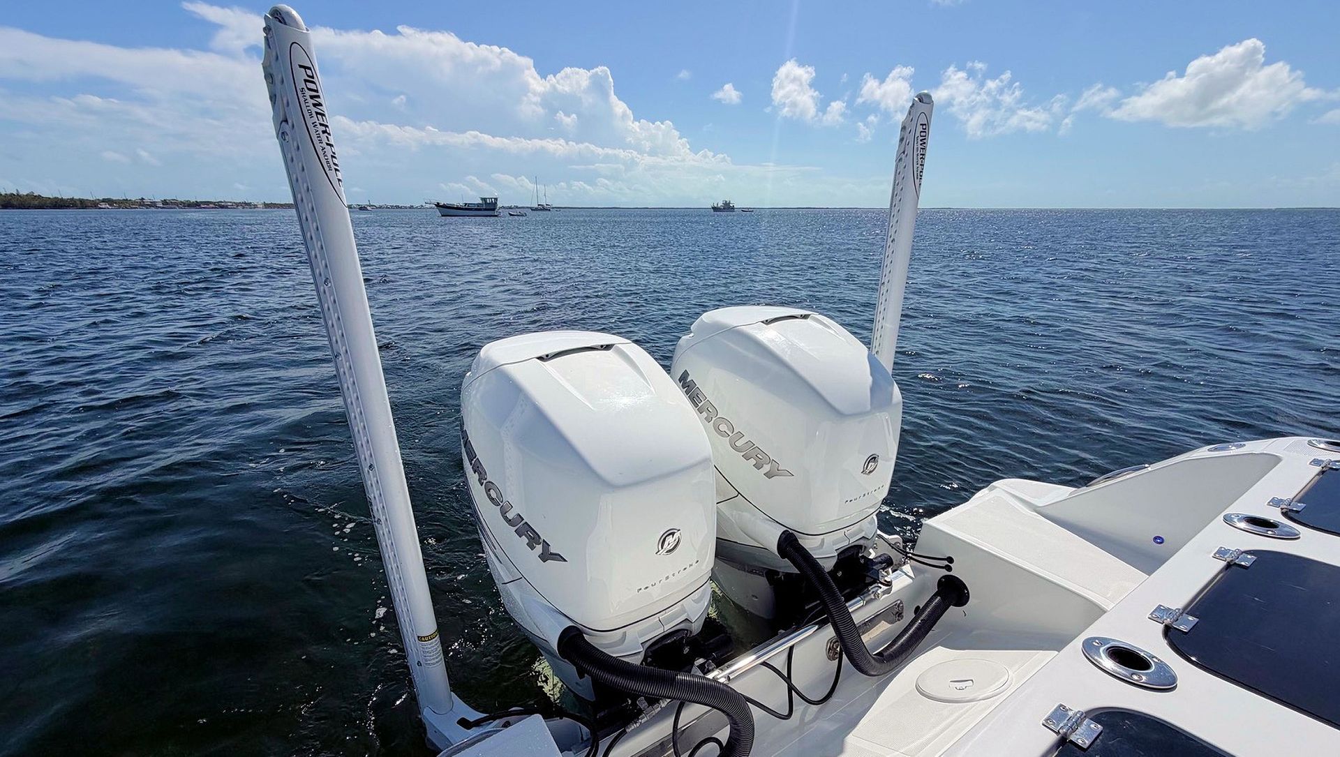 Two white outboard motors on a boat, with open blue water and cloudy sky in the background.