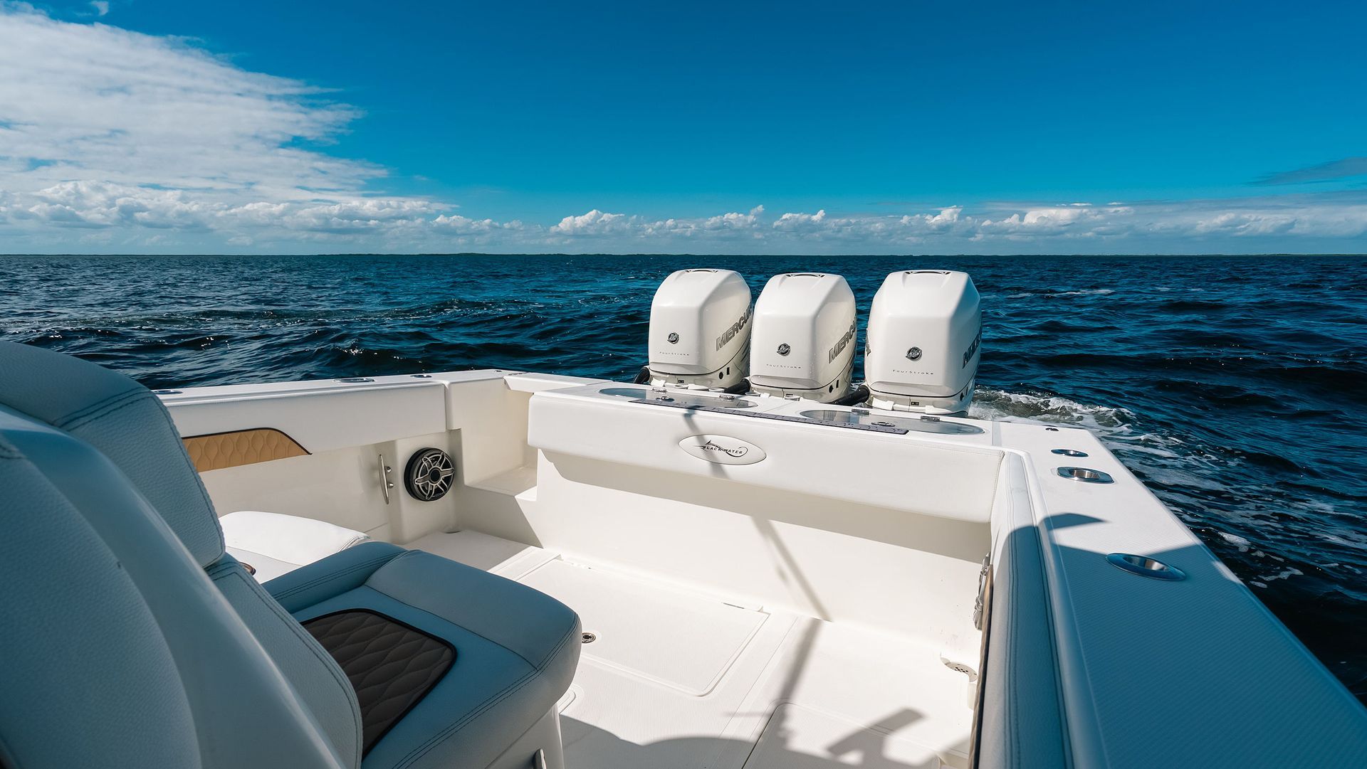 White boat seating and three outboard motors on open ocean under a blue sky