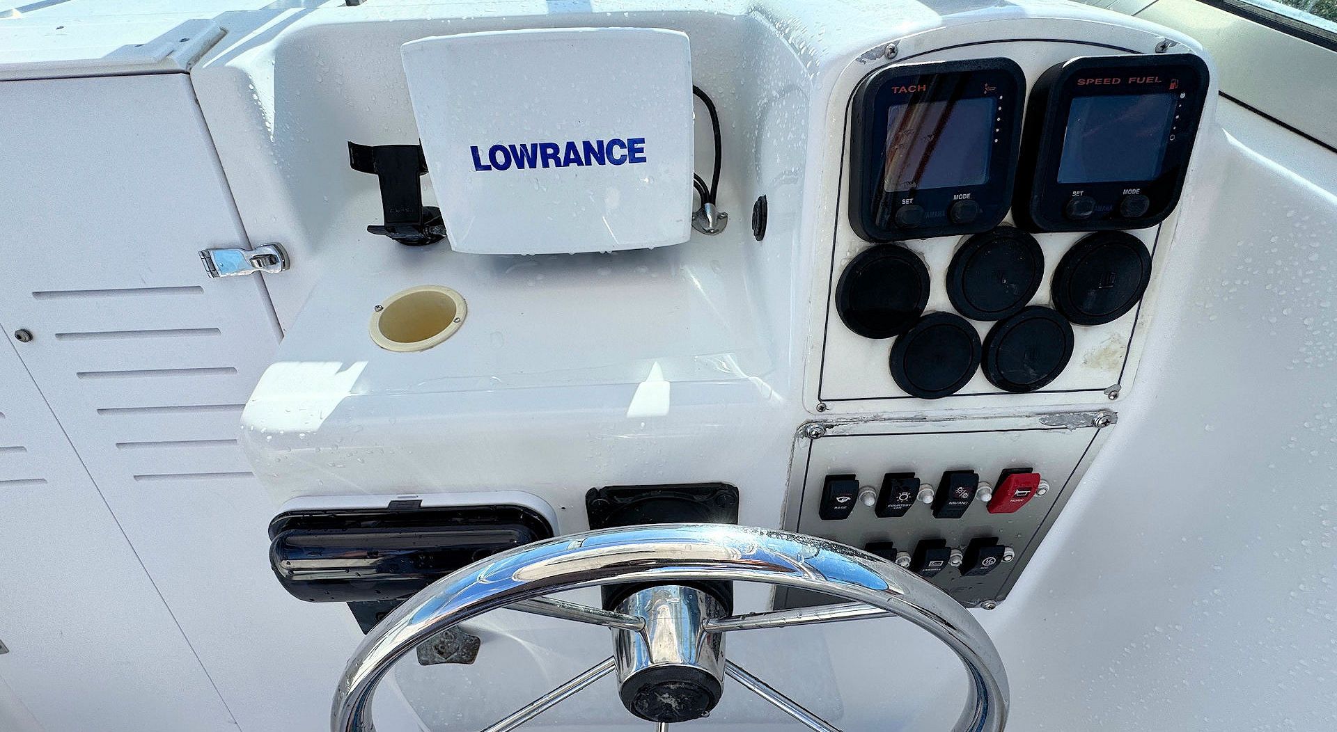The boat helm console features a Lowrance display, dual gauges, a steering wheel, and a panel of switches.