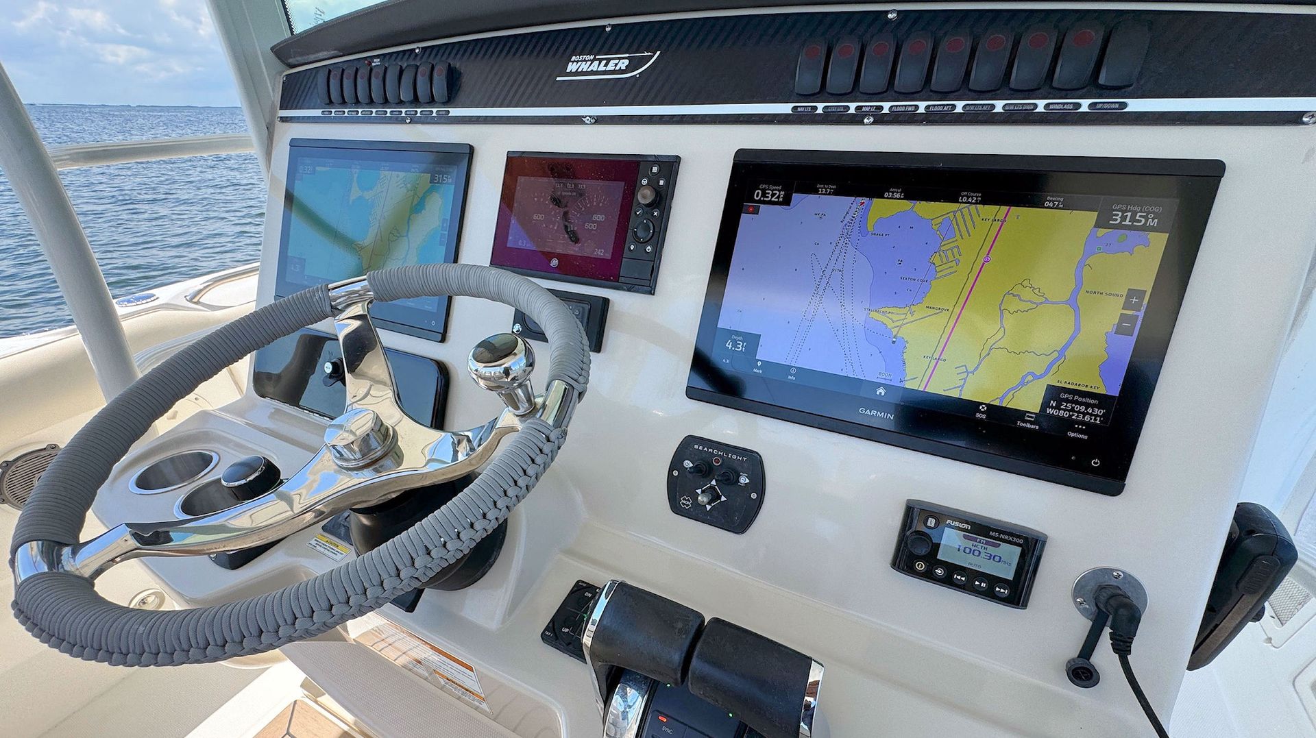 Boat helm with steering wheel, navigation screens, and controls on a bright day at sea