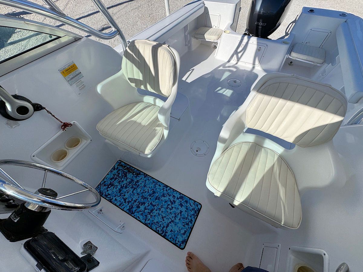 Interior of a white boat with two cushioned seats, a steering wheel, and a blue speckled floor mat.