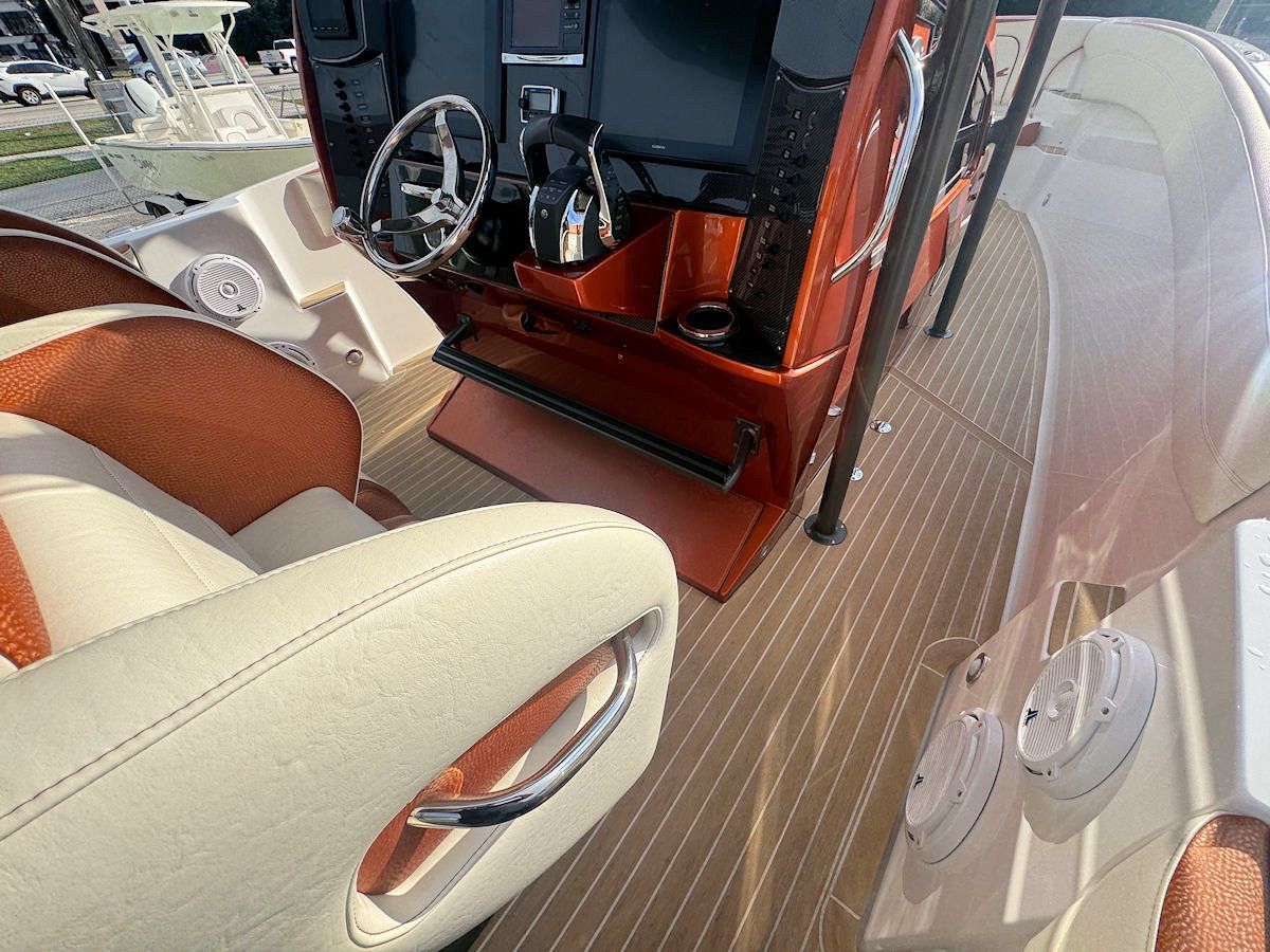 View of a boat's interior with orange and beige accents, featuring steering wheel, seats, and wood-like flooring.
