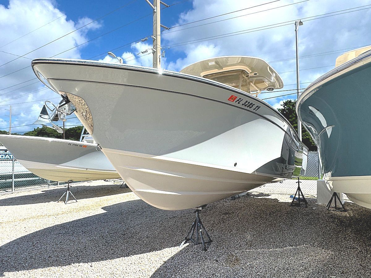 White motorboat with tan hull, on stands in a lot, sunny day.