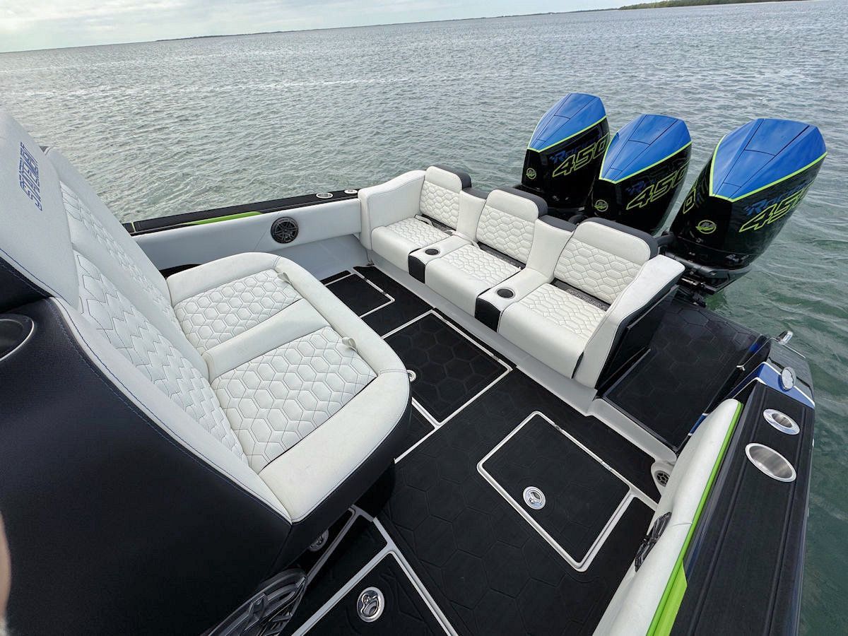 View from the stern of a boat with white and black seating, black flooring, and three blue outboard motors.