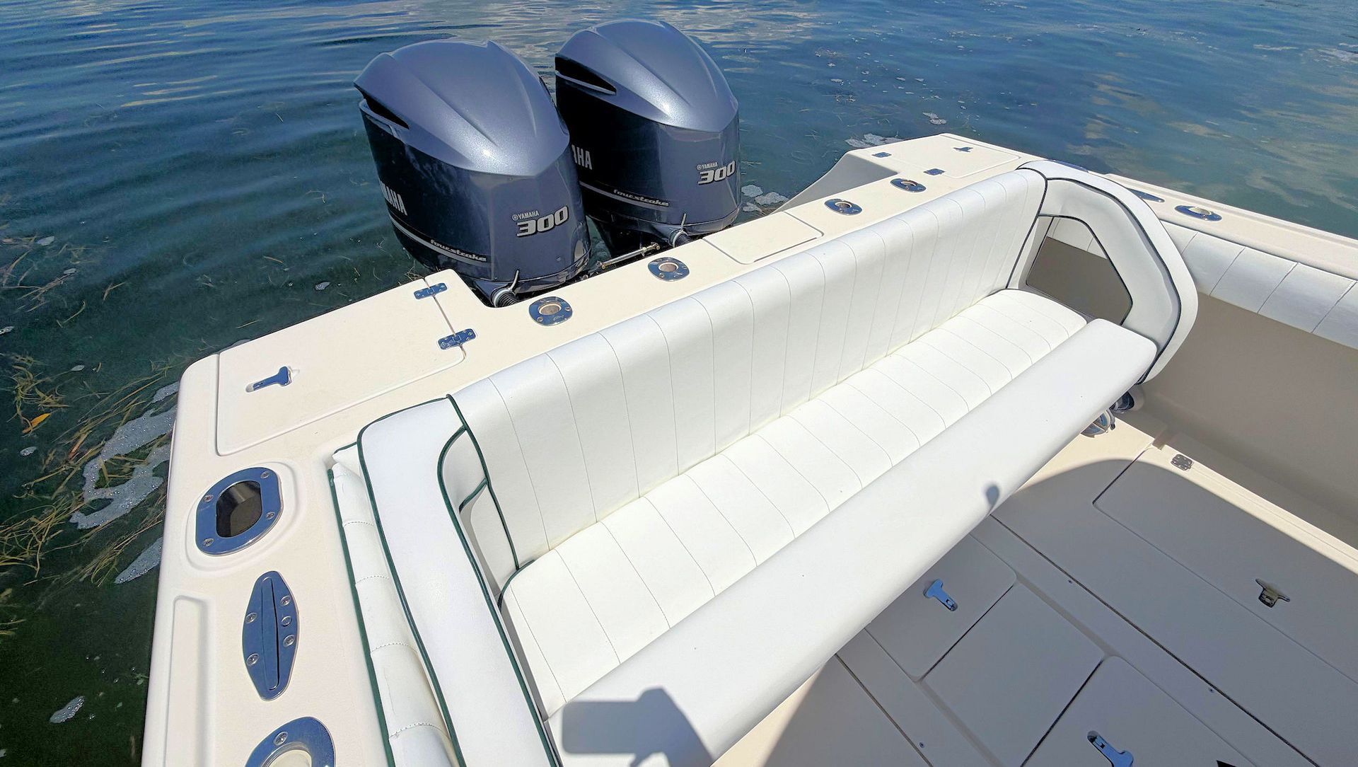 White cushioned boat seating beside twin outboard motors on a yacht stern above the water