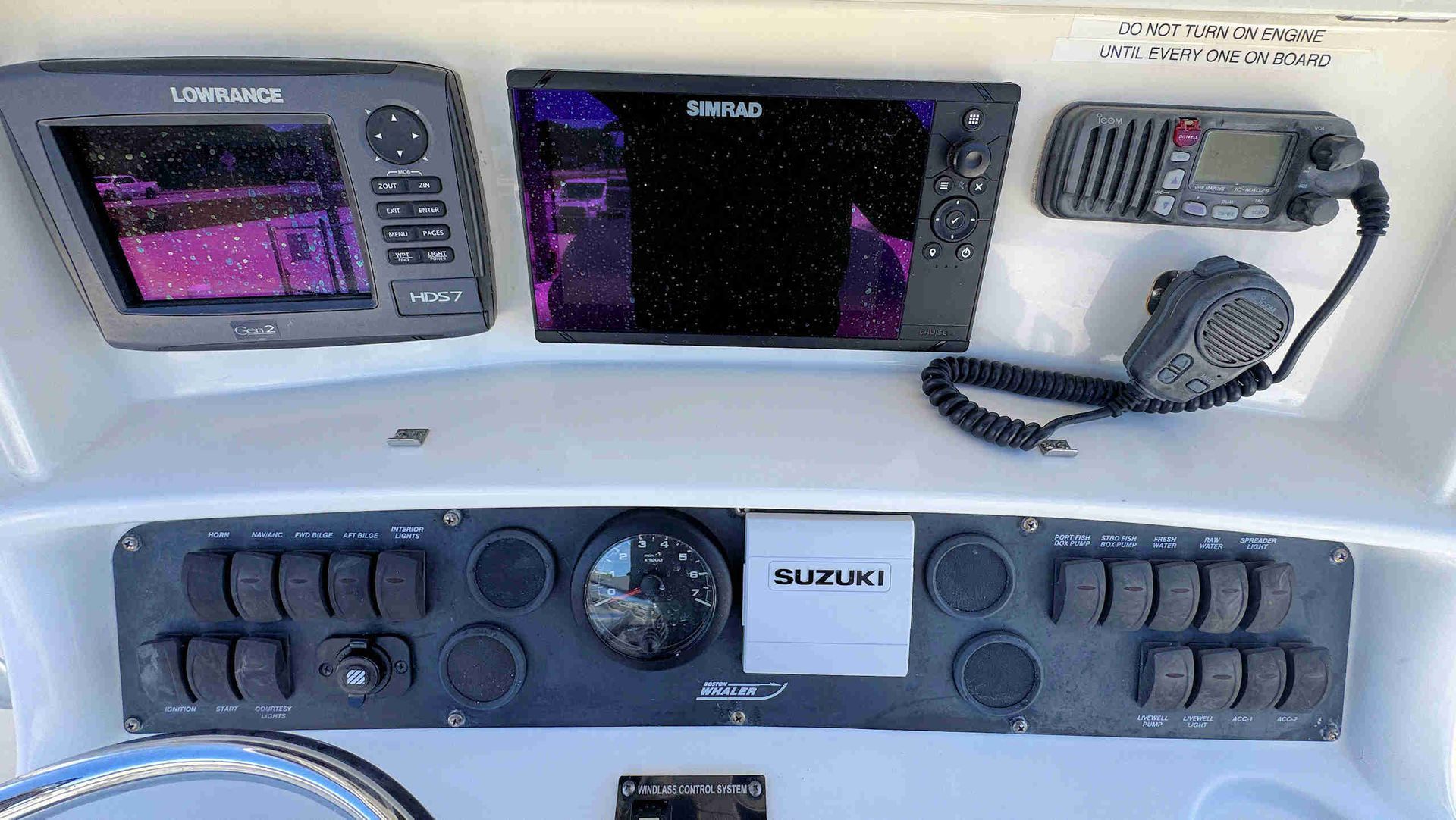 Boat helm with dual marine displays, radio handset, gauges, and Suzuki controls on a white console