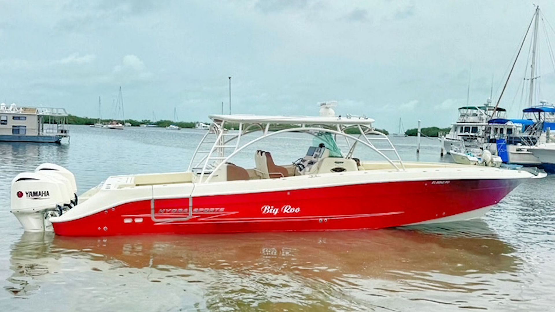 Red center console boat on calm water near a marina, with people aboard under a white canopy.