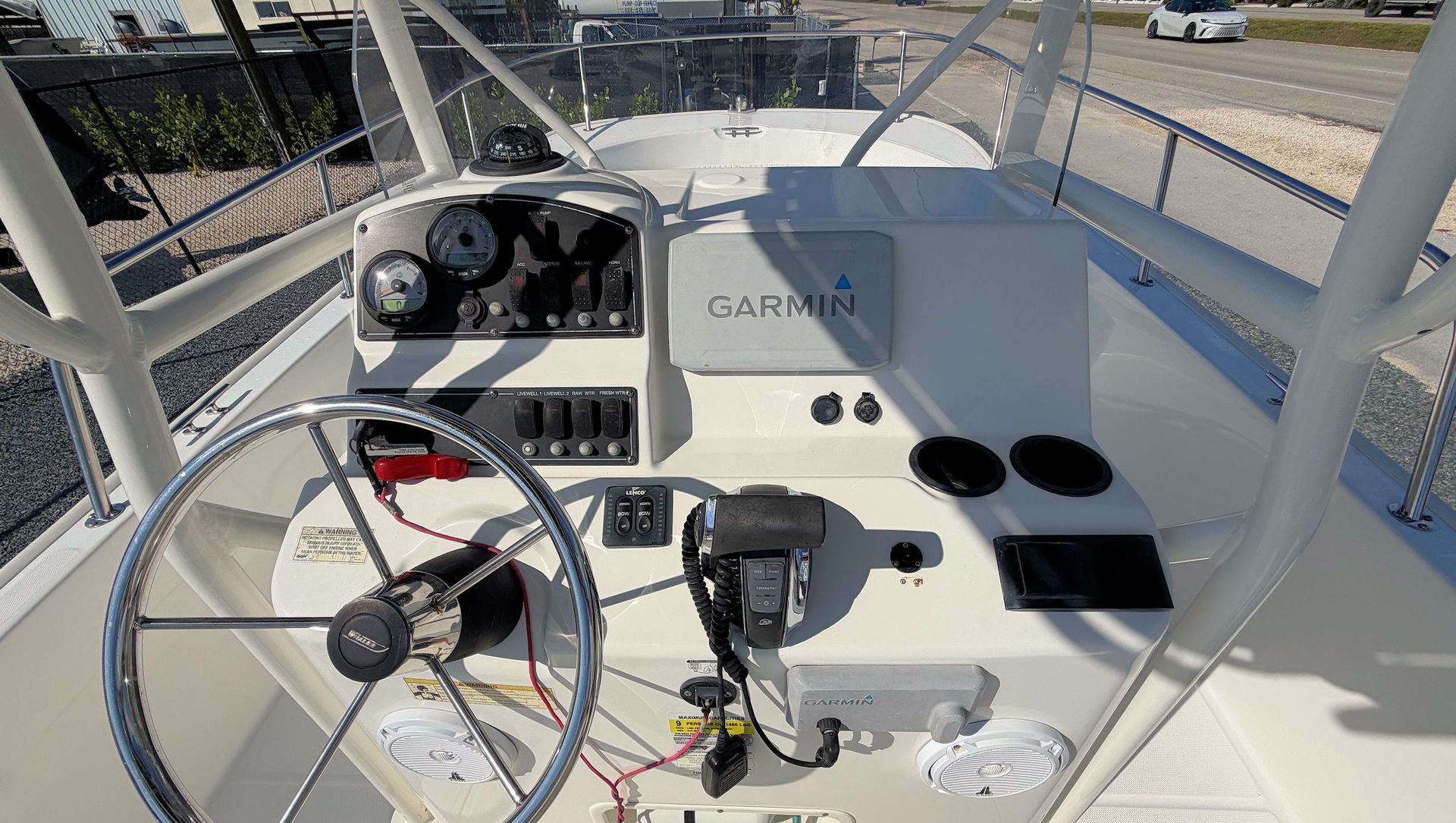 Boat helm with steering wheel, gauges, radio, and controls on a sunny deck.