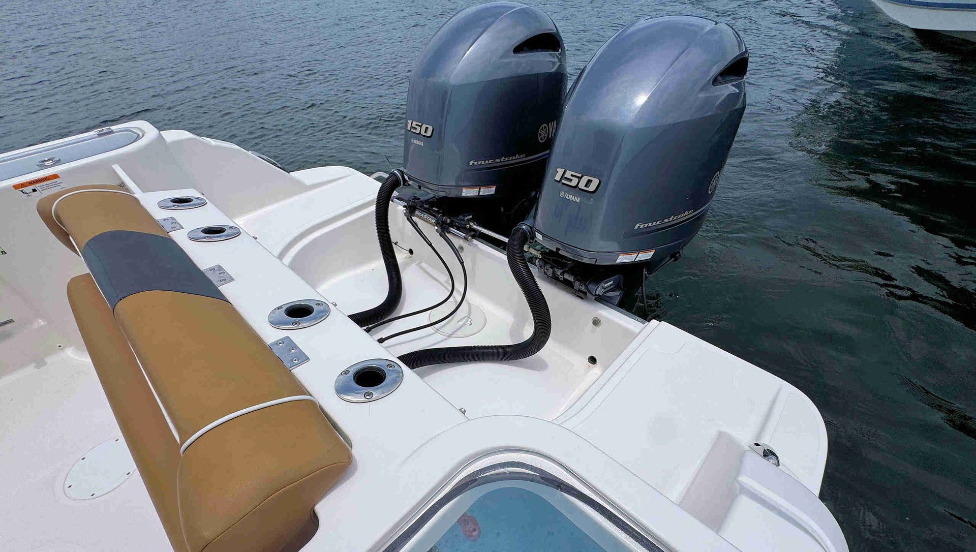Boat stern with twin gray outboard motors, tan seat, and fishing rod holders on calm water