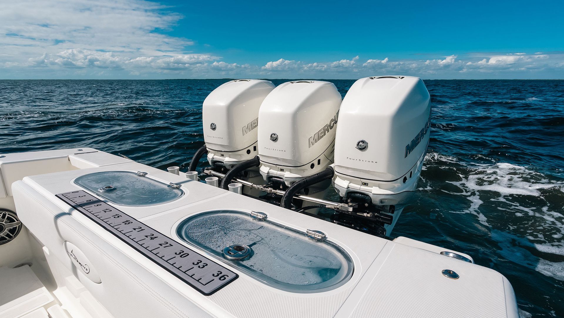 White boat stern with three outboard motors on open blue ocean.
