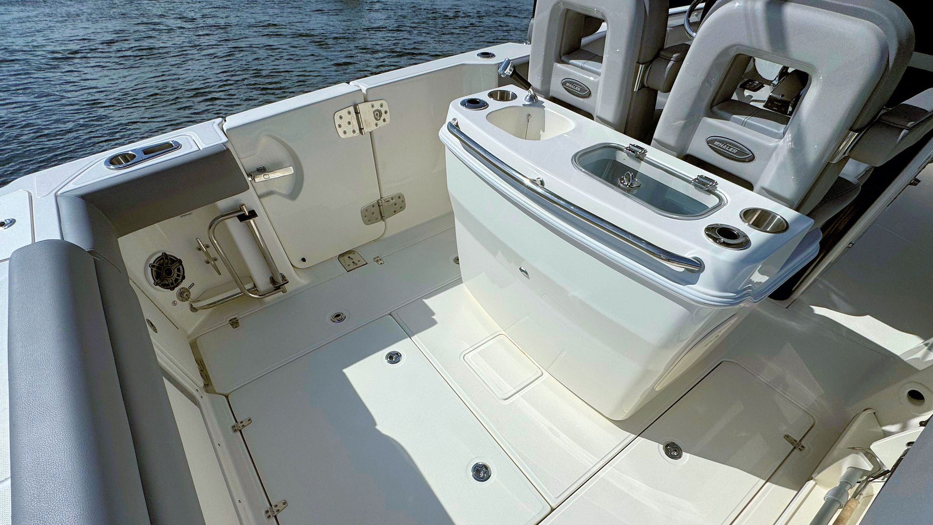 The deck of a white fiberglass boat featuring a central seating console with a built-in bait tank and cupholders.