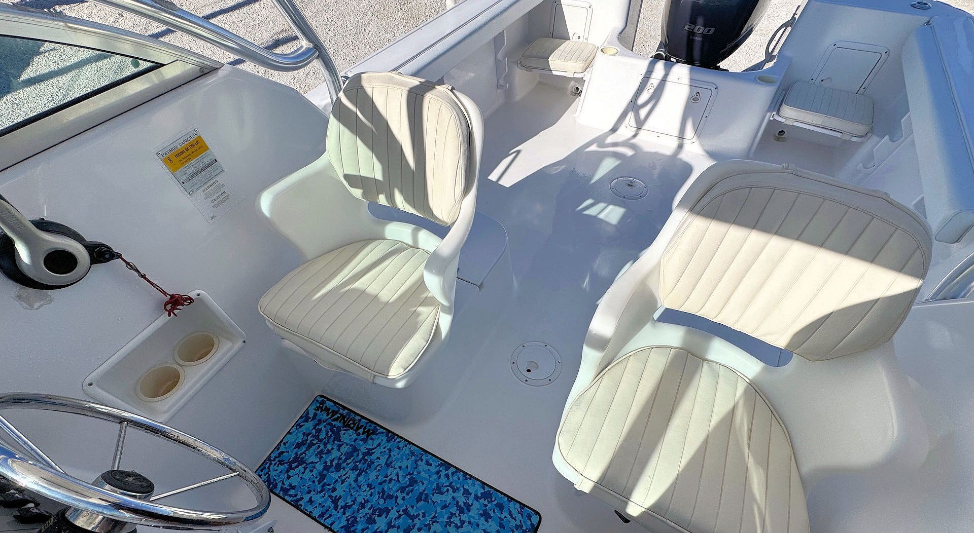 The cockpit of a white boat, showing two beige captain’s chairs, a steering wheel, and a blue patterned floor mat.