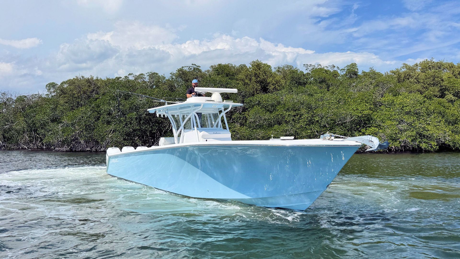 Light blue center console boat on clear water near mangrove shoreline under a blue sky.